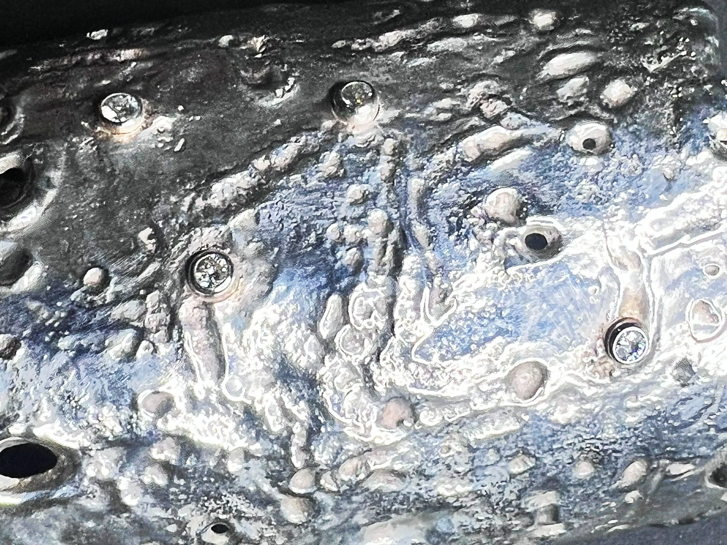 Close-up of a metallic surface with various bumps, holes, and rivets, showing a textured, shiny, and rough appearance.