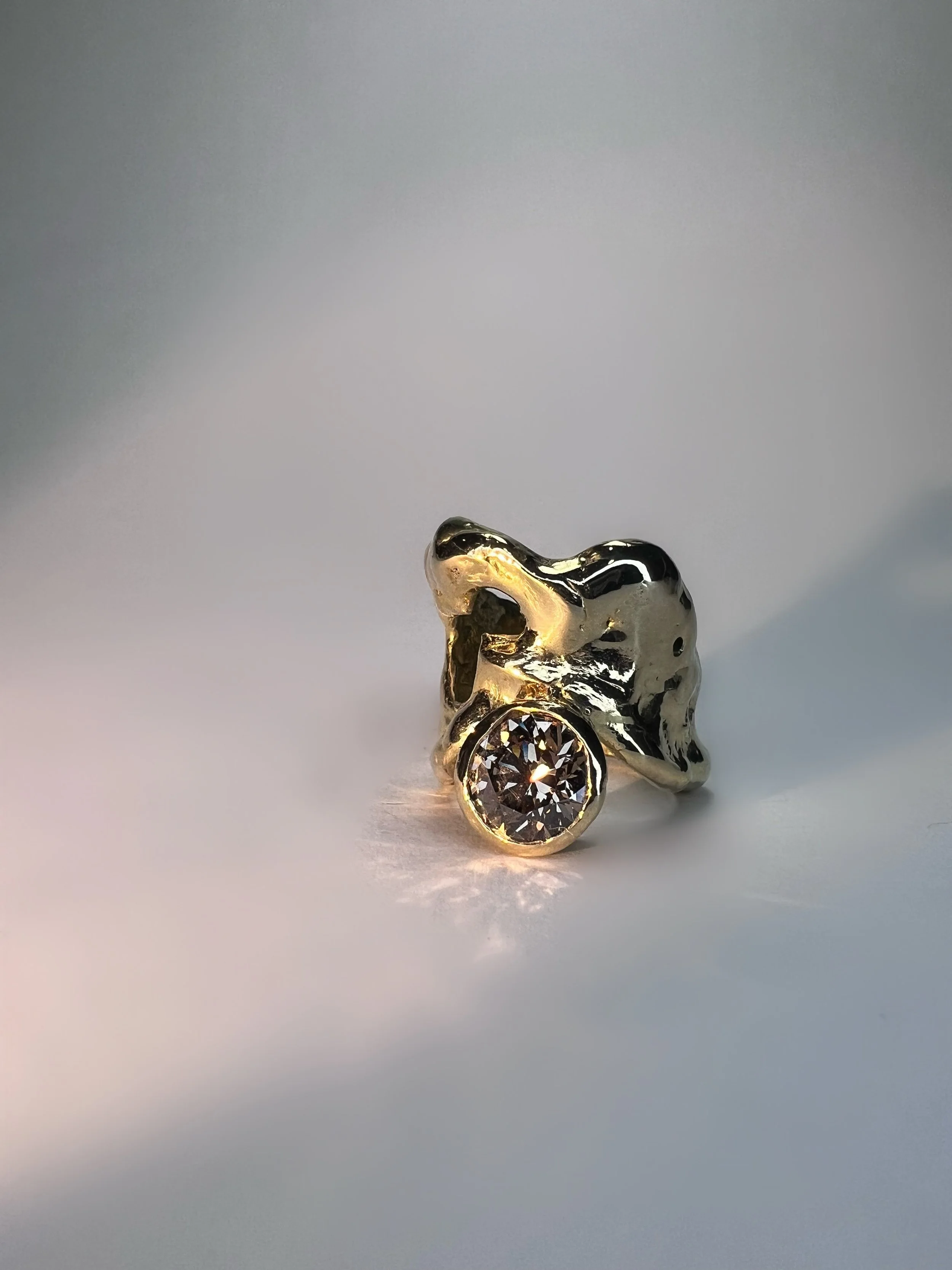 A small, shiny, metallic object with a clear, round gemstone at its base, placed on a plain, neutral background.