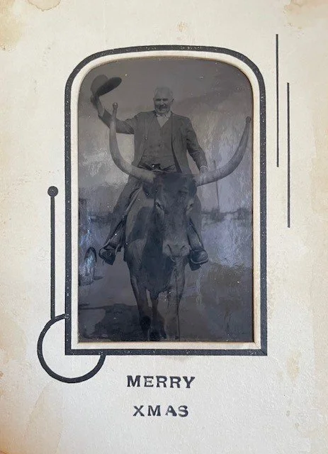 Black and white photograph of a man riding a buffalo, holding a hat high, with the text 'Merry Xmas' below.