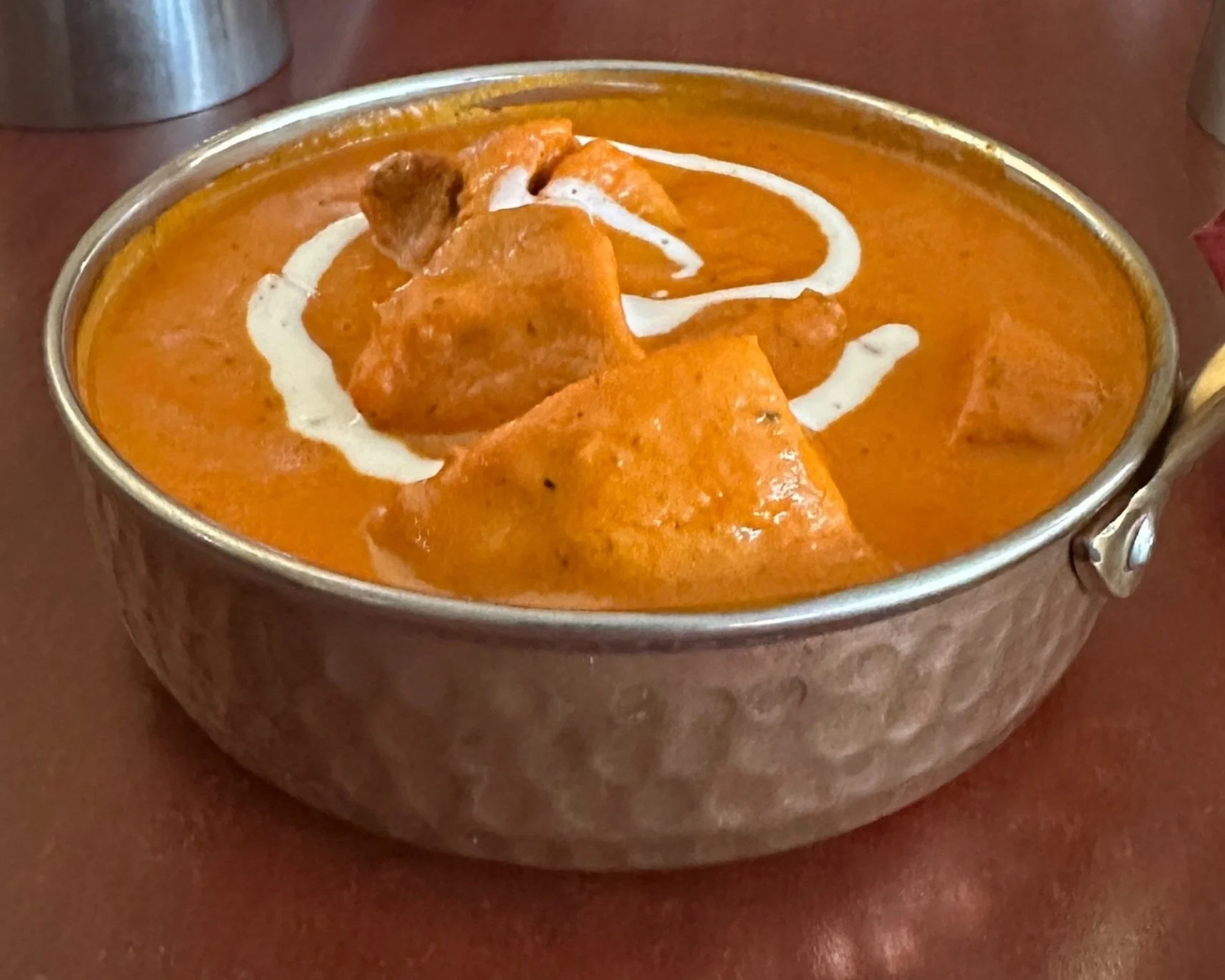 A bowl of Indian butter chicken curry with pieces of chicken in an orange sauce, garnished with a drizzle of cream.