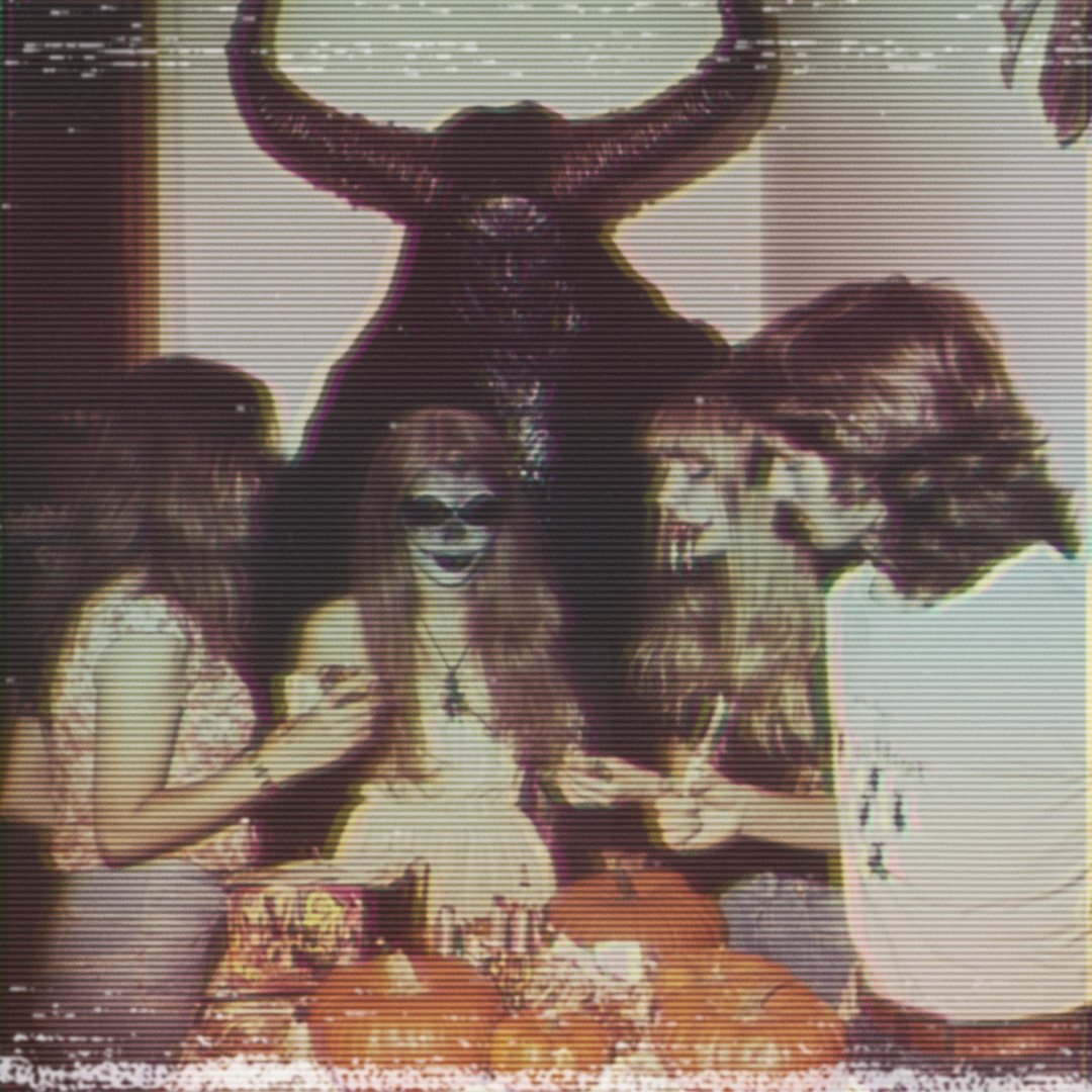 Vintage photo of a group of people with painted faces and a horned statue in the background, surrounded by Halloween decorations and pumpkins.