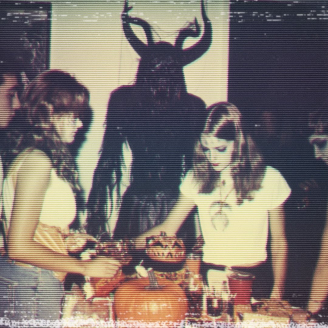 Party scene with vintage effect; two women near a table with pumpkins and bowls, and a person in a horned costume in the background.