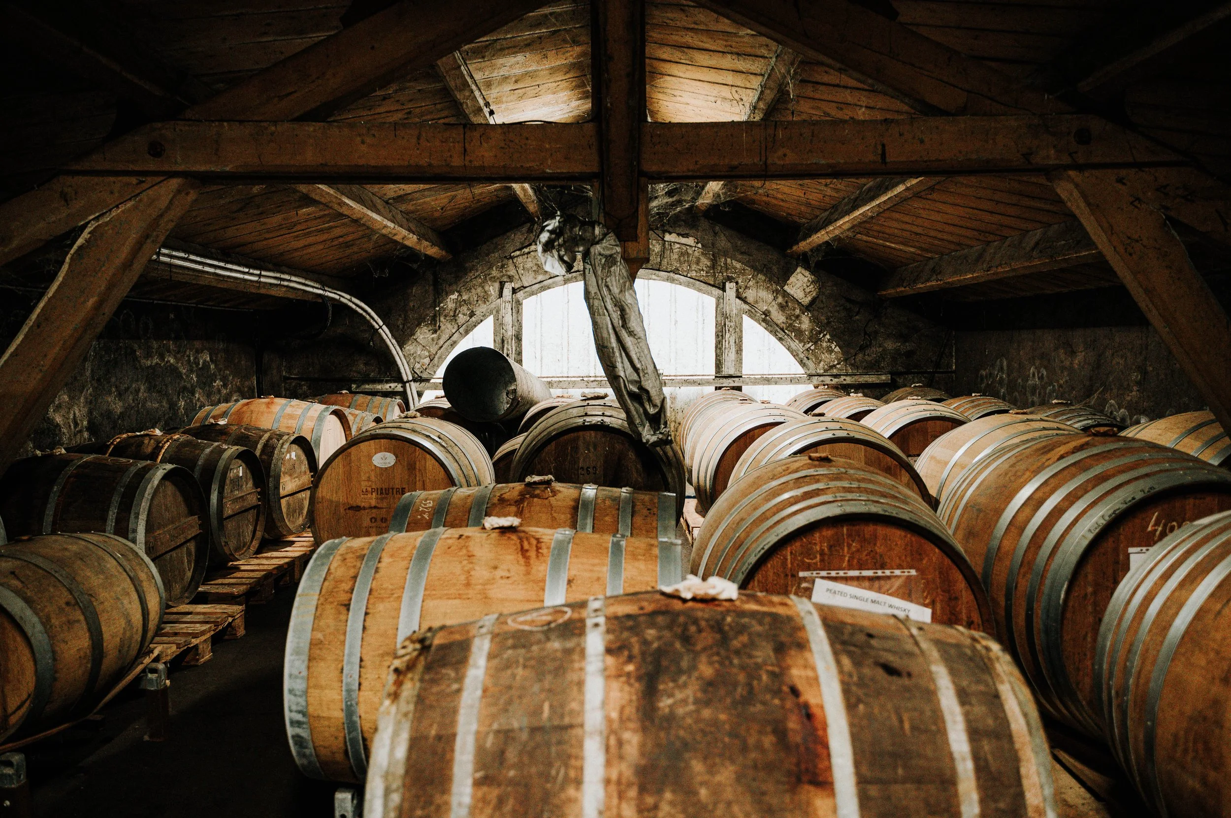 Fûts de whisky en chêne dans une cave de vieillissement en pierre avec une fenêtre en arrière-plan