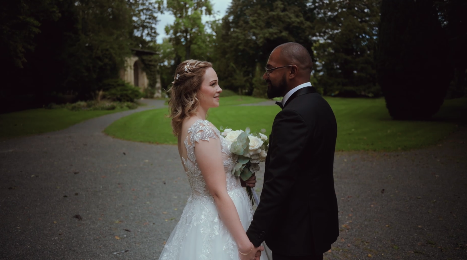 Un couple de mariés se tenant par la main et se regardant avec amour dans un parc verdoyant.