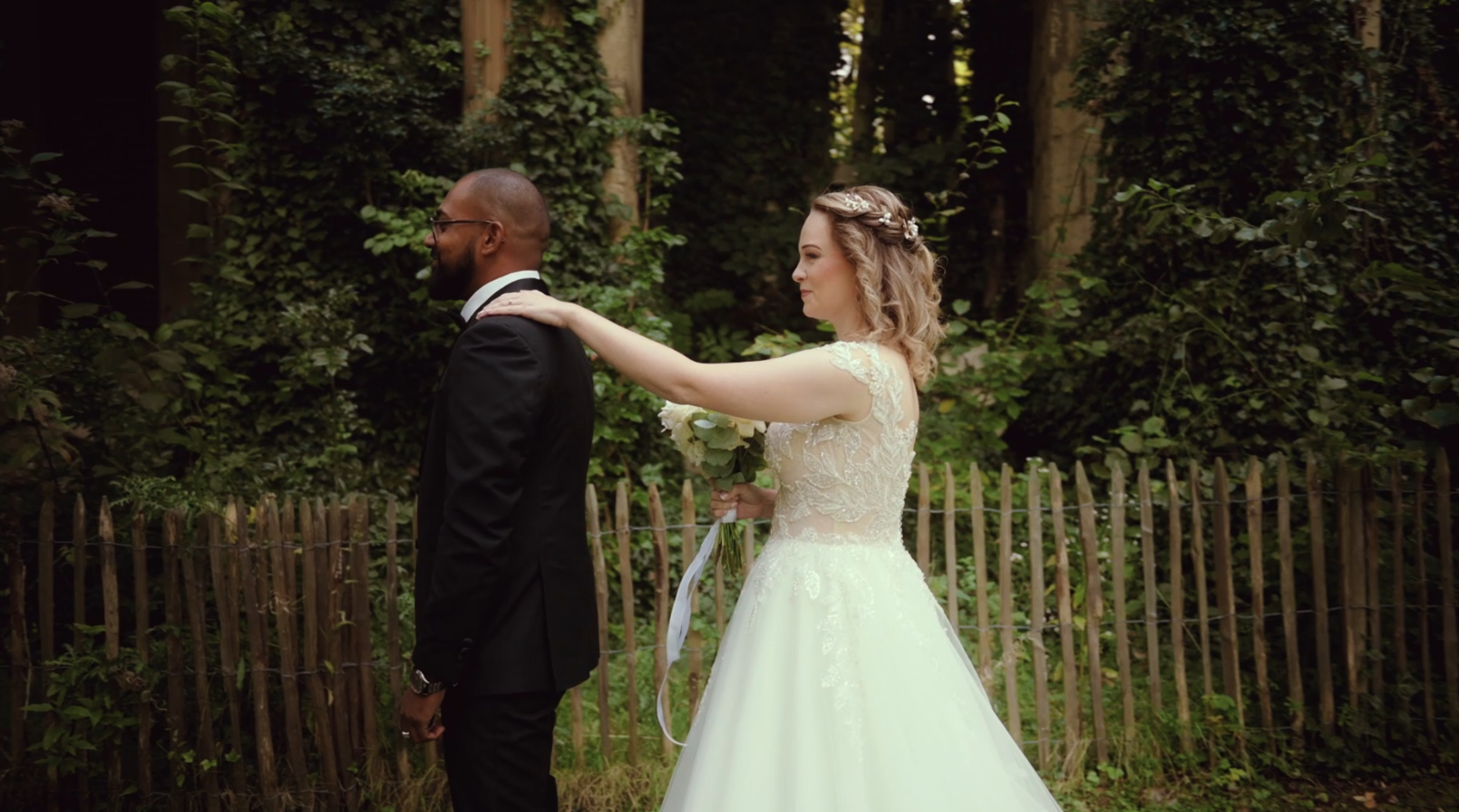 Un couple lors de leur mariage, la mariée touche le dos du marié dans un jardin.