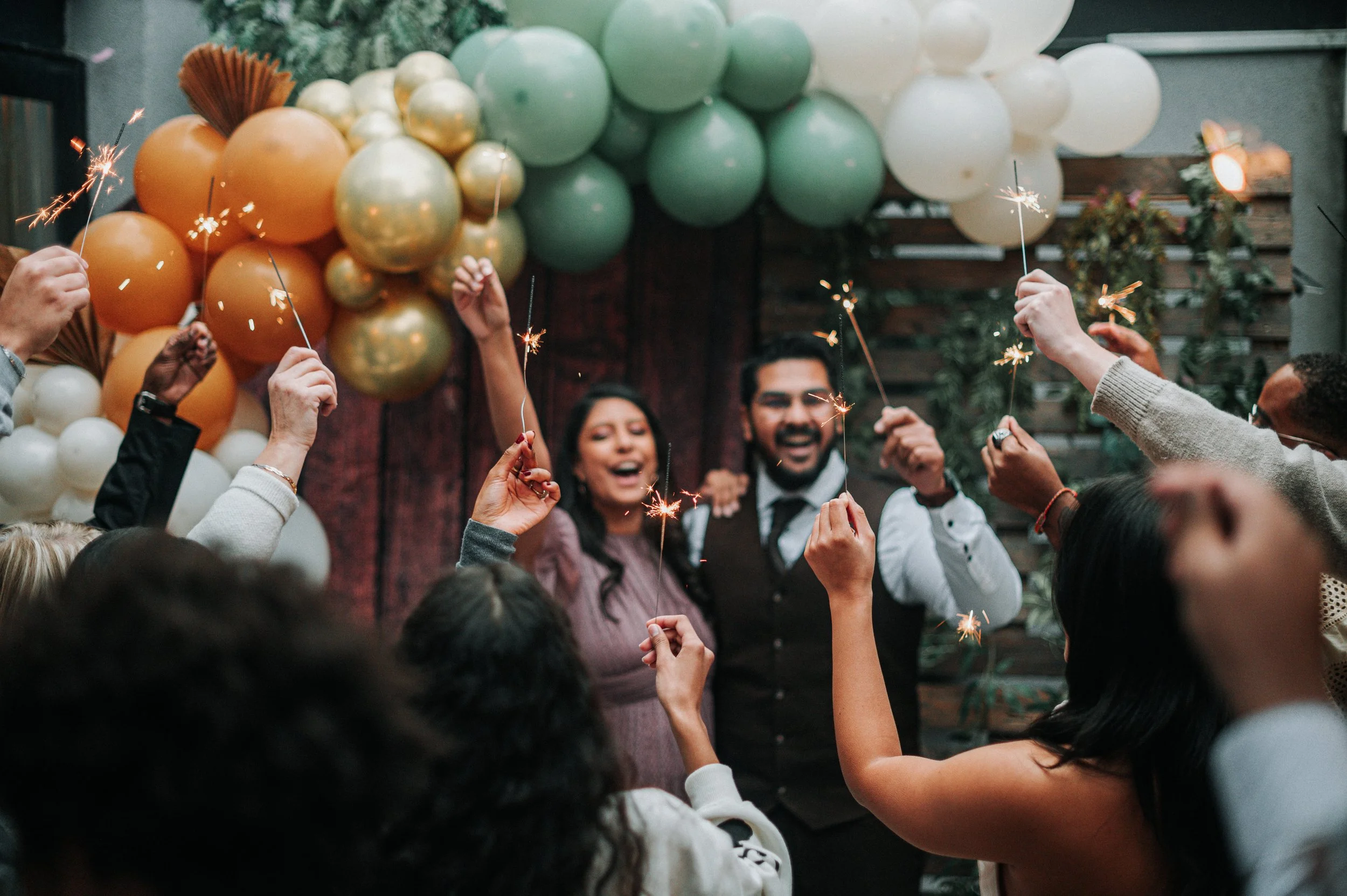 Groupe de personnes célébrant avec des feux de Bengale lors d'une fête, avec des ballons décoreux en arrière-plan.