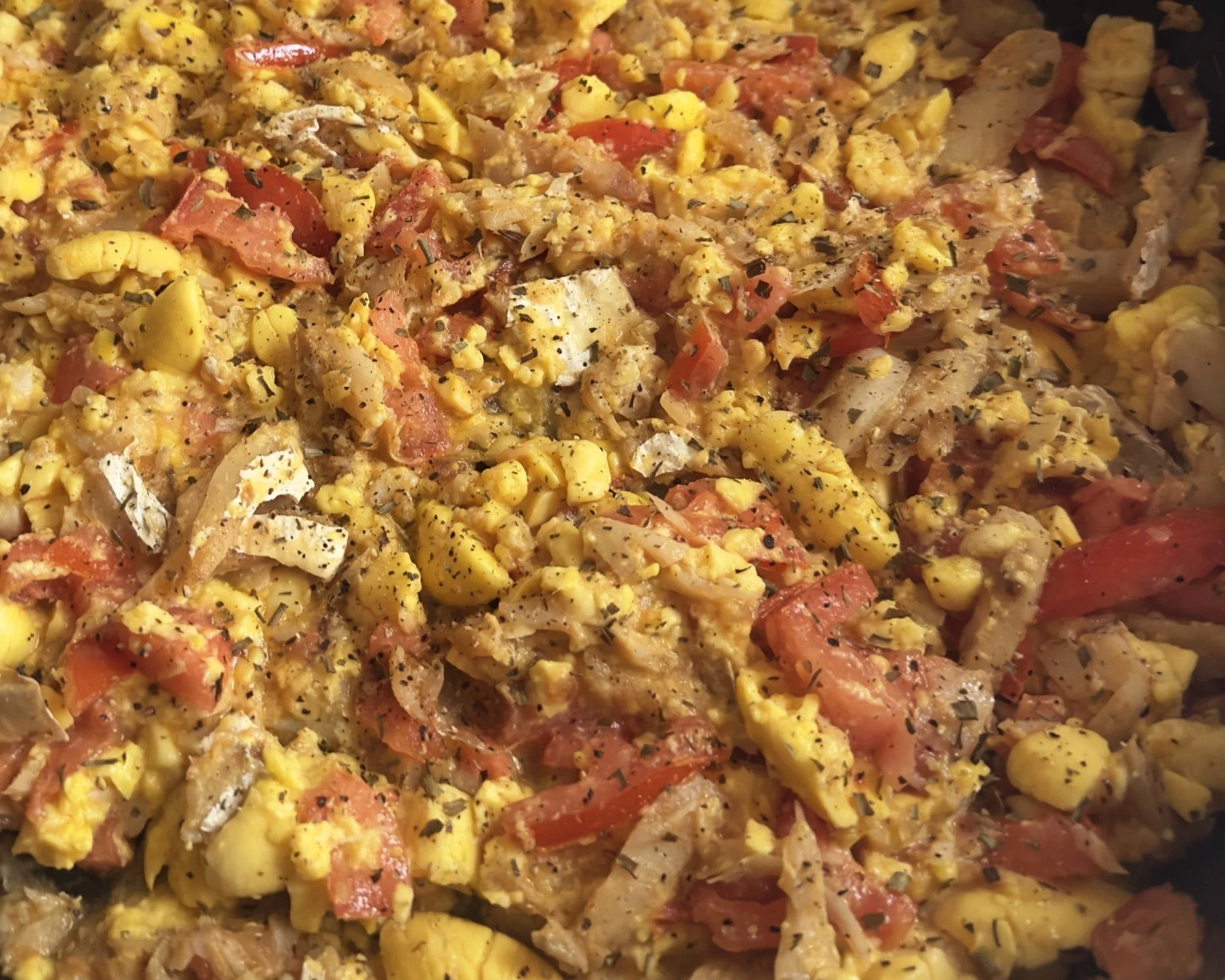 Close-up of scrambled eggs with tomatoes, herbs, and black pepper.
