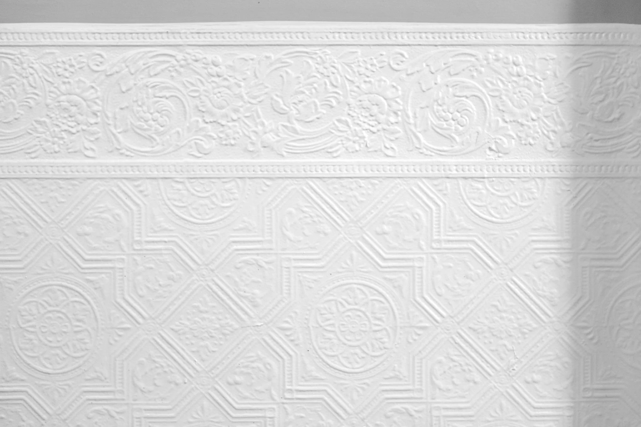 Close-up of an ornate textured white wall with floral and geometric patterns.