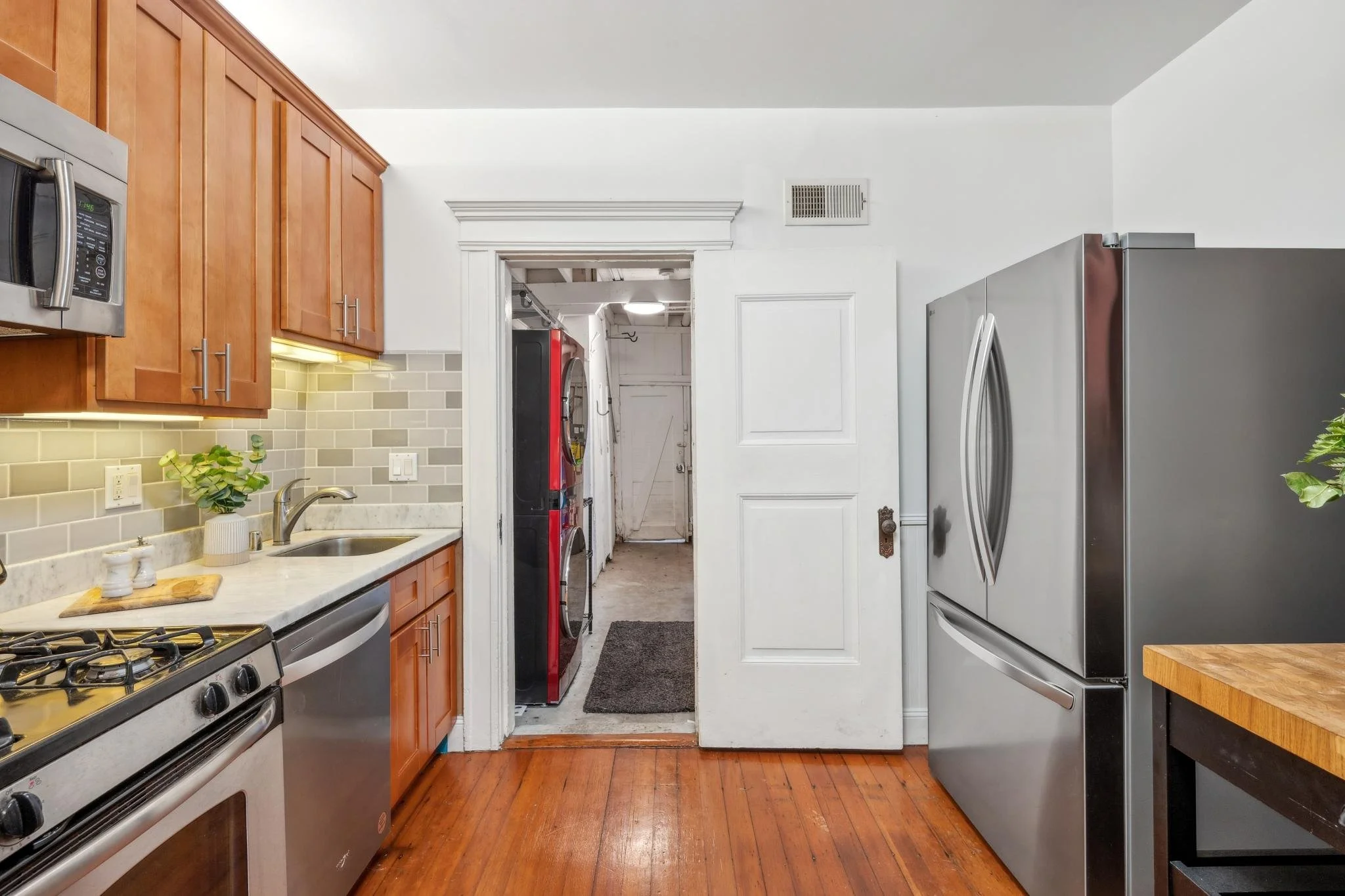 Kitchen with wooden cabinets, stainless steel appliances, gray tile backsplash, white countertop, and a doorway leading to a laundry area with a stacked washer and dryer.