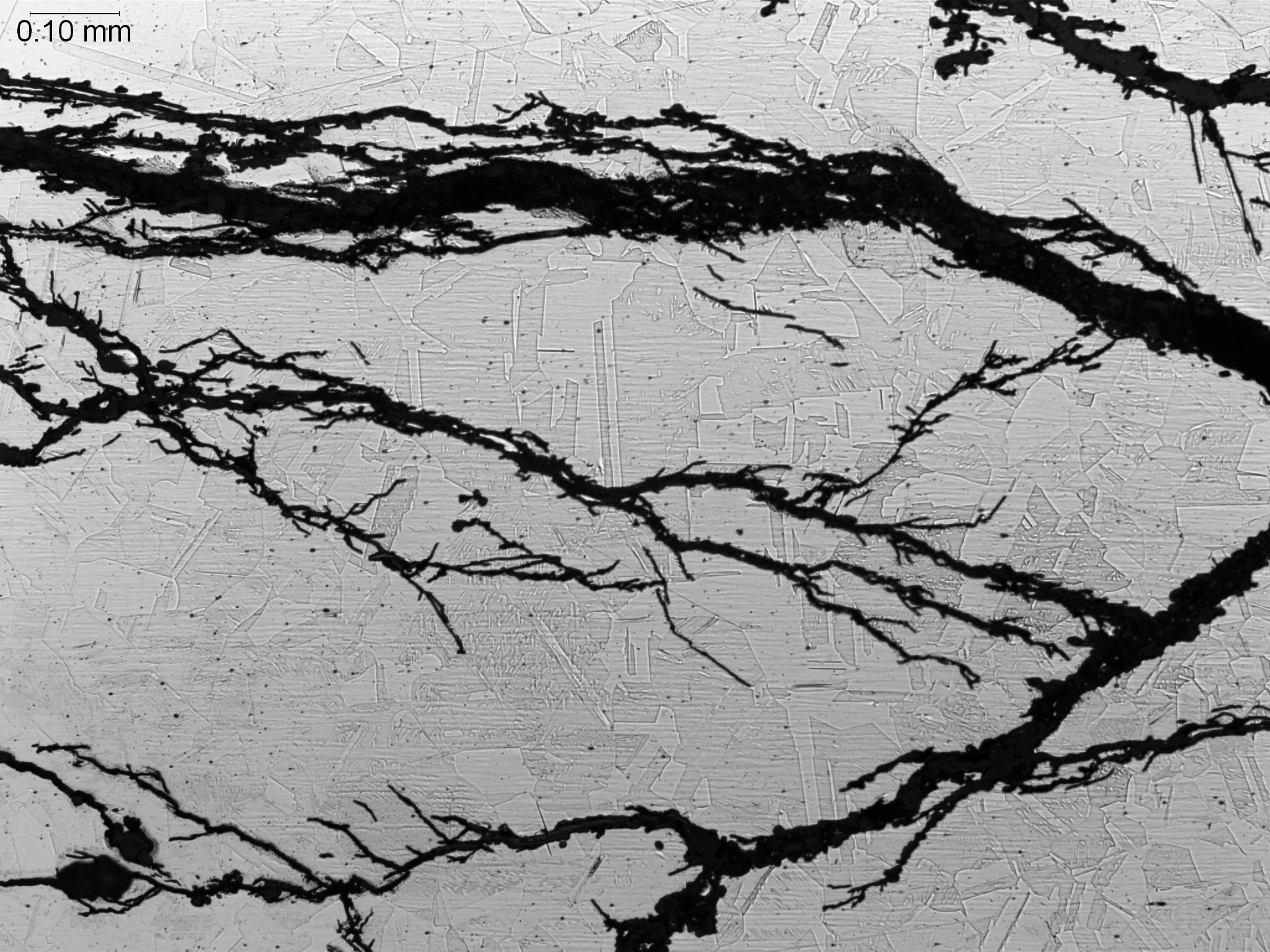 SCC (Stress Corrosion Cracking) in stainless steel hot water pipe 100x, metallographic cross-sectional evaluation identifying highly branched transgranular stress corrosion cracking SCC paths, crystalline grain penetration networks, and an etched equ