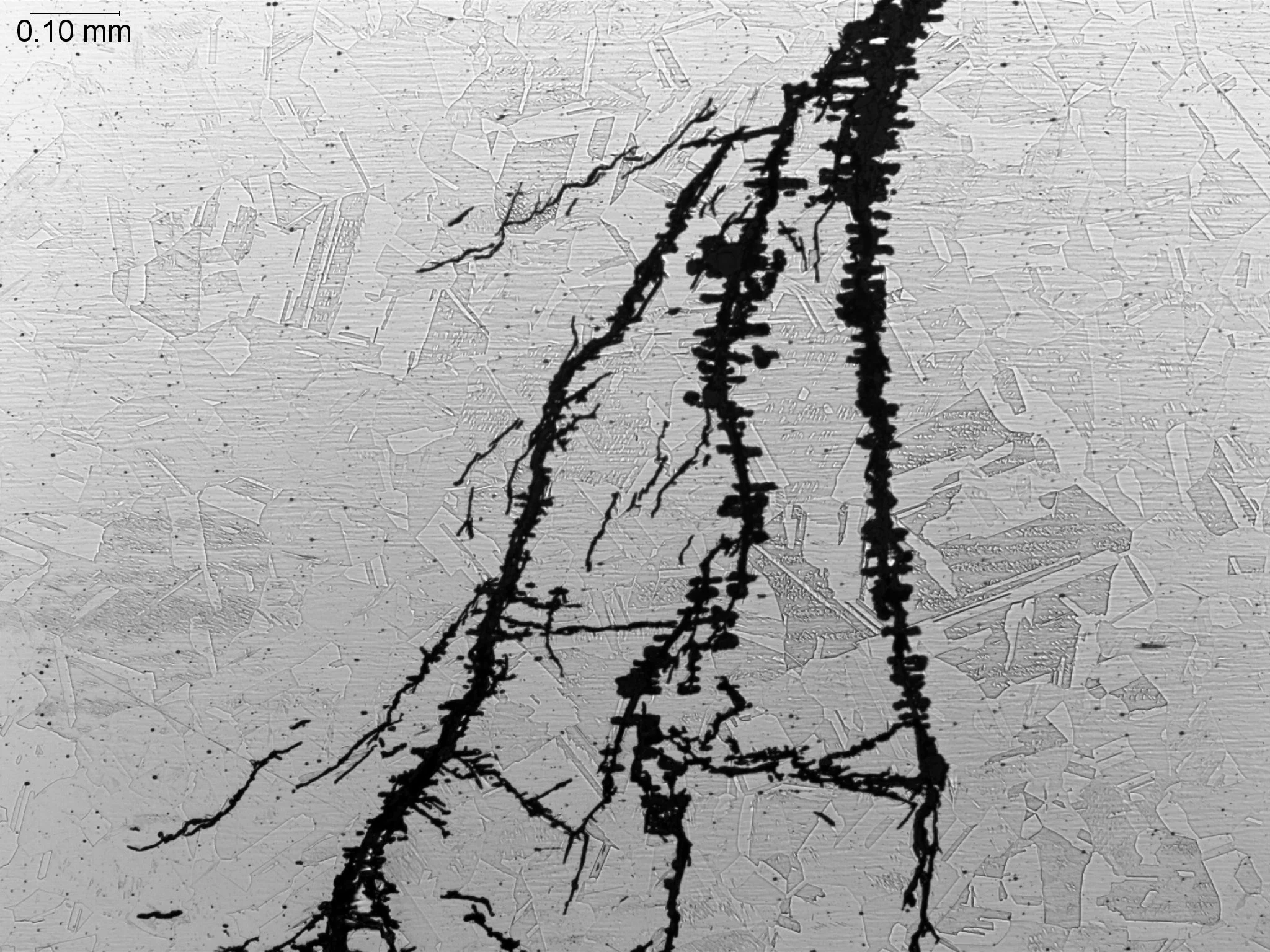 Microbiologically Influenced Corrosion (MIC) in a stainless steel hot water pipe at 100x magnification, metallographic cross-sectional evaluation identifying localized biocorrosion pitting, tunneling subsurface cavity propagation tracks, and an etche