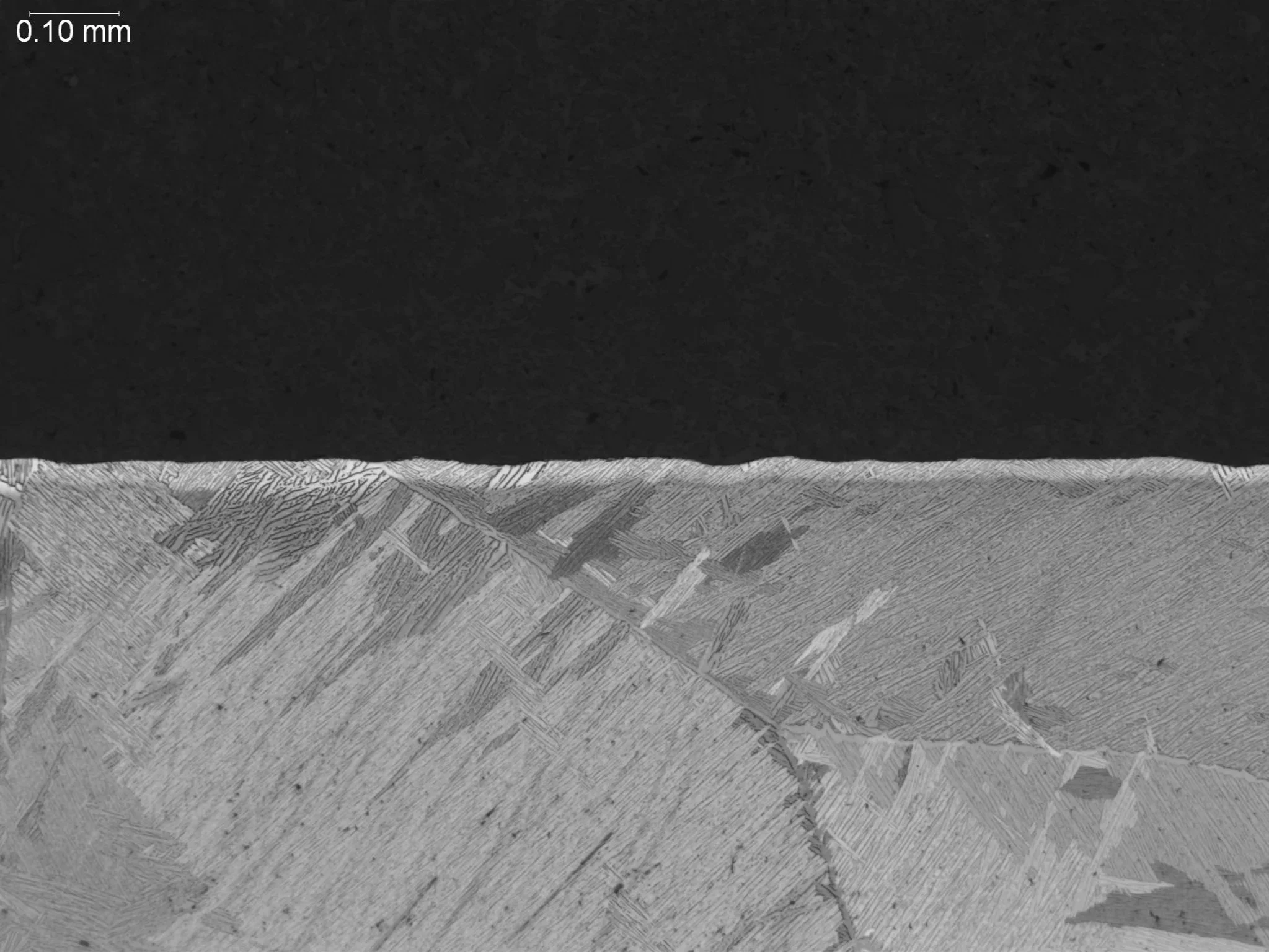 Alpha case on cast titanium at 100x magnification, metallographic cross-sectional evaluation identifying a continuous surface contamination layer, brittle alpha-stabilized casing morphology, and an underlying acicular alpha-beta matrix structure per 