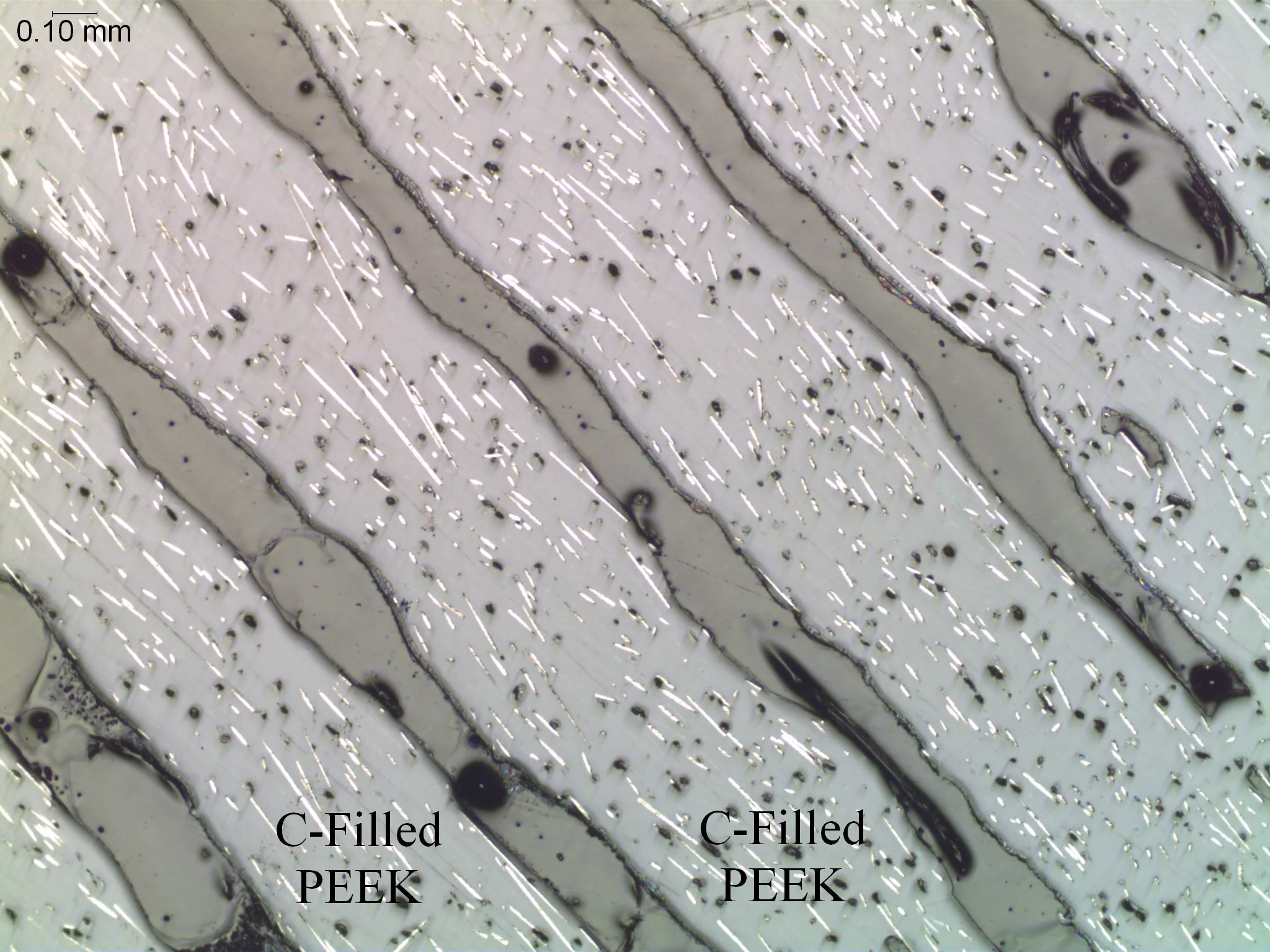 Inter-laminar delamination in a carbon-fiber-reinforced composite matrix, microstructural cross-sectional evaluation identifying polymer interface voiding, carbon-filled PEEK layer distribution, and structural layer separations per ASTM E2015 and AST