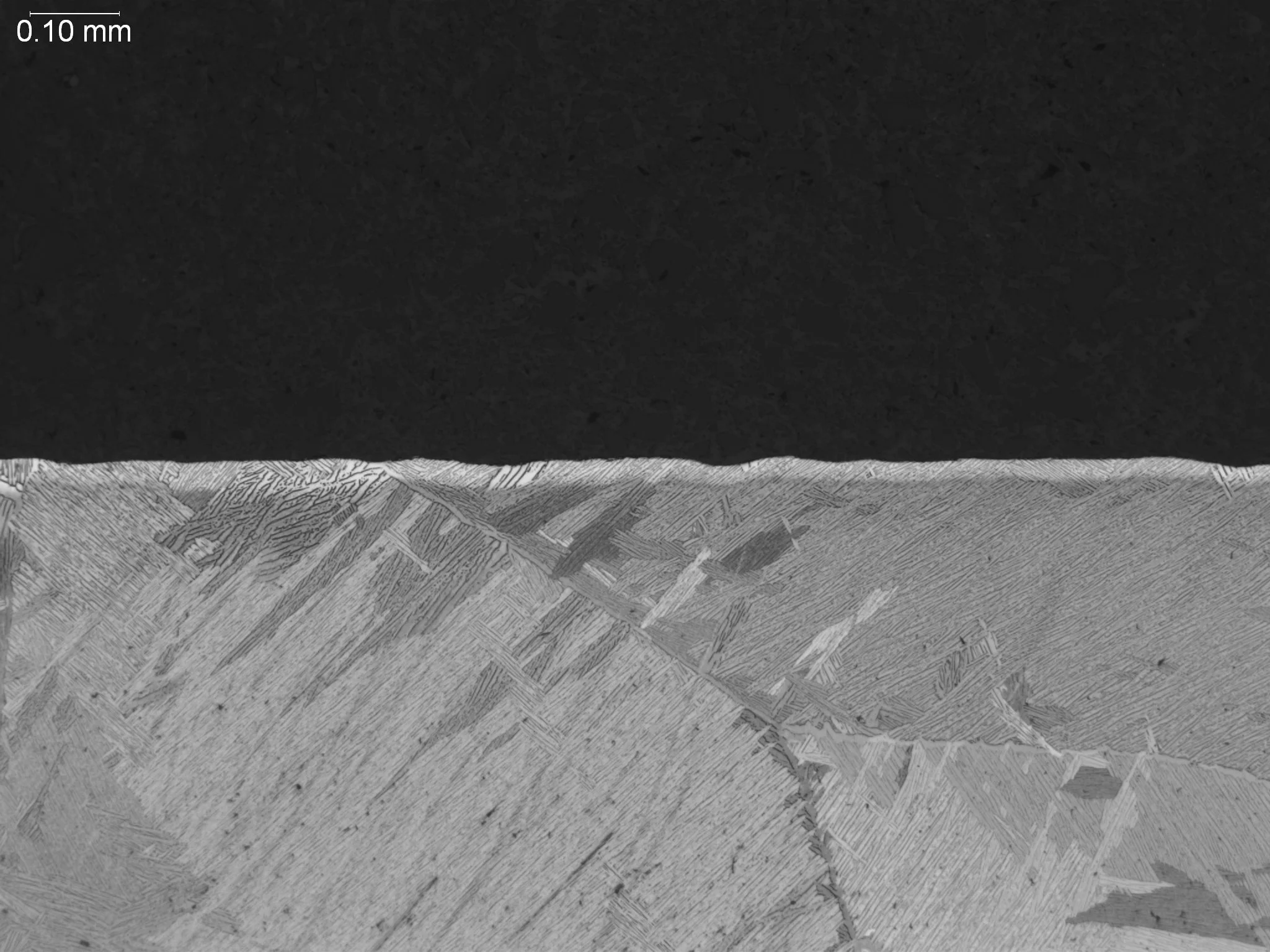 Alpha case on cast titanium at 100x magnification, metallographic cross-sectional evaluation identifying a continuous surface contamination layer, brittle alpha-stabilized casing morphology, and an underlying acicular alpha-beta matrix structure per 