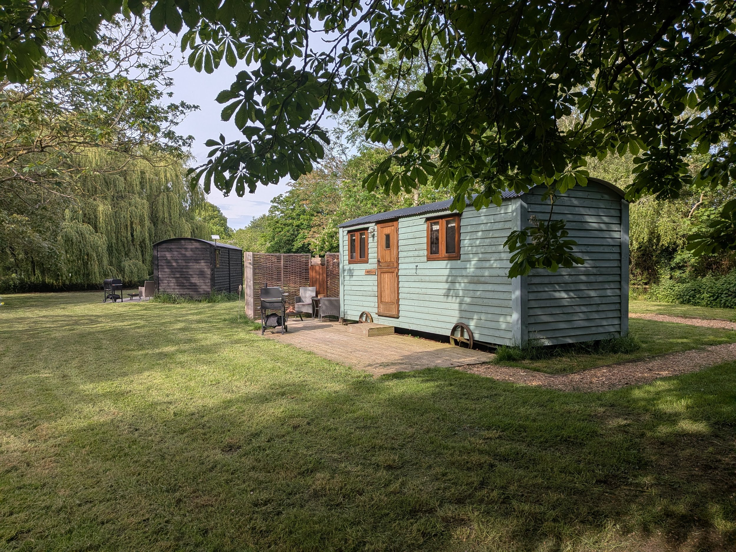 Photo of a backyard with trees and grass, featuring two small trailers and outdoor furniture.