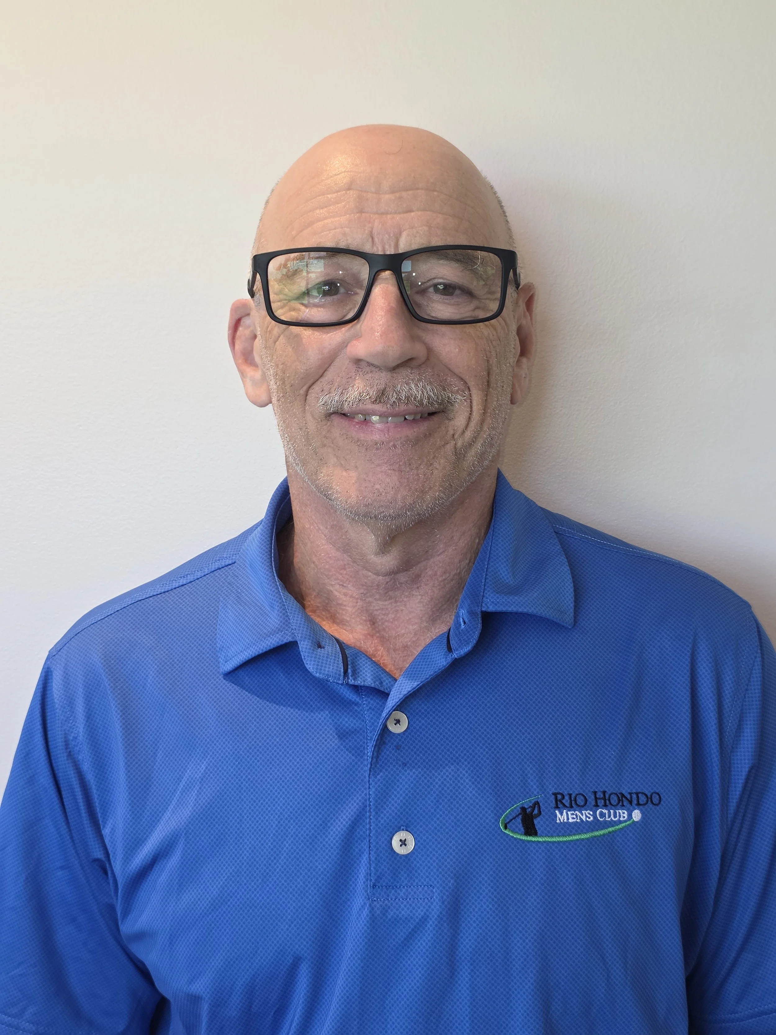 Man wearing a black Rio Hondo Men's Club shirt, smiling at the camera, against a plain background.