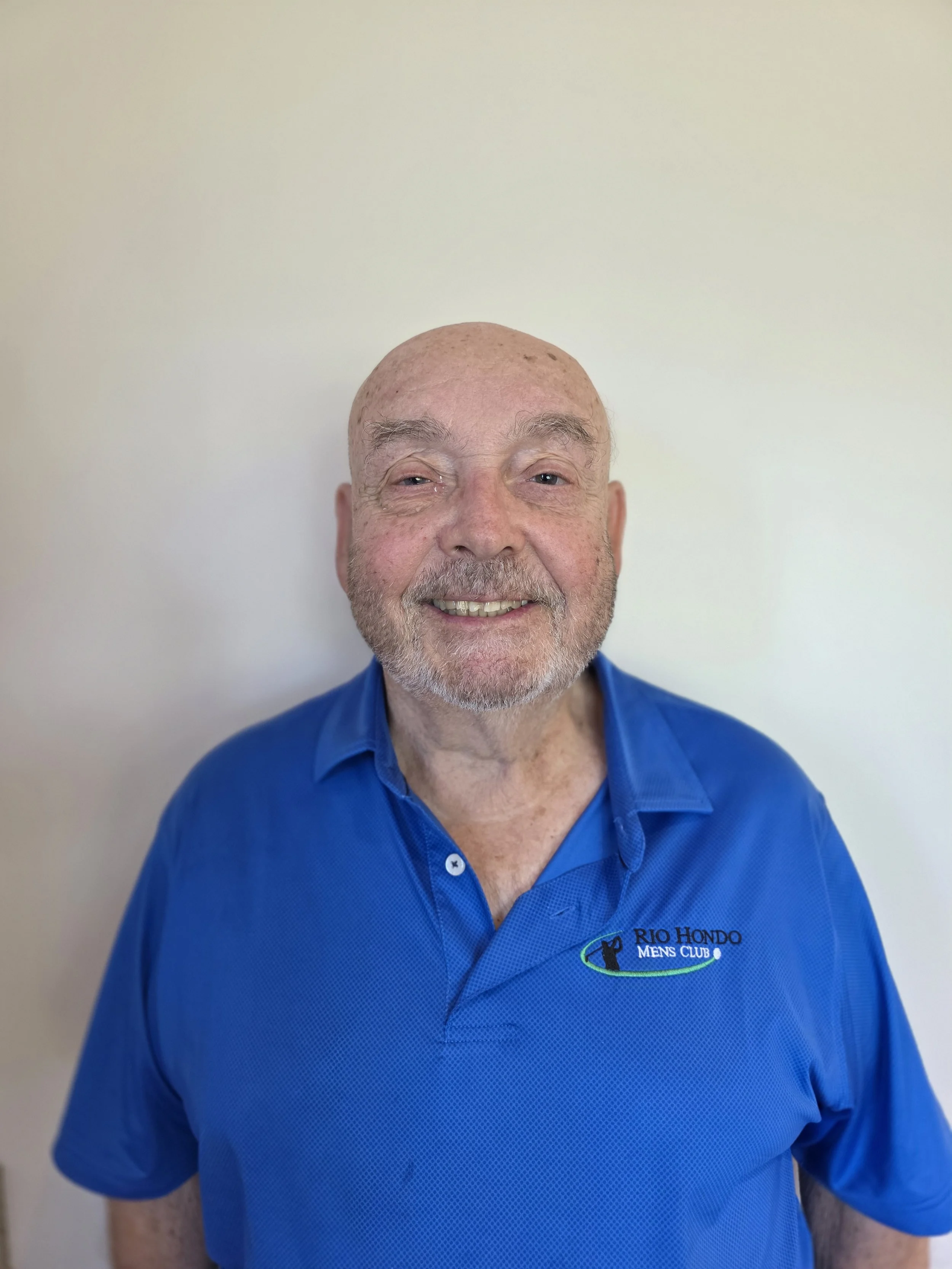 Smiling man wearing a black "Rio Hondo Men's Club" polo shirt, cap, and sunglasses resting on the cap.