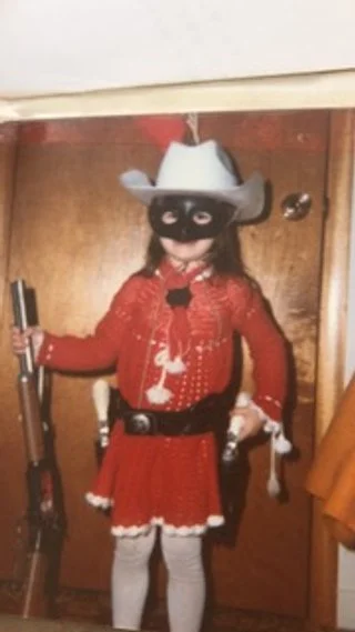 Child dressed in a costume with a red dress, a white cowboy hat, and a face mask.