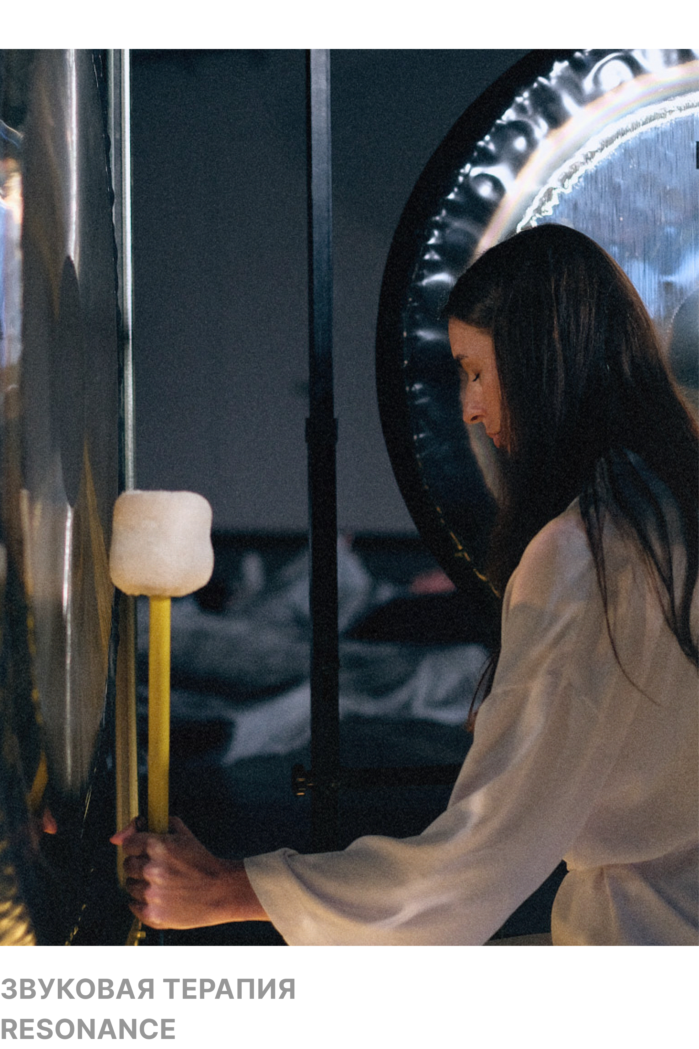 A woman with long dark hair is pressing a large button or switch on a wall, with her head bowed down and eyes closed, in a dimly lit room.