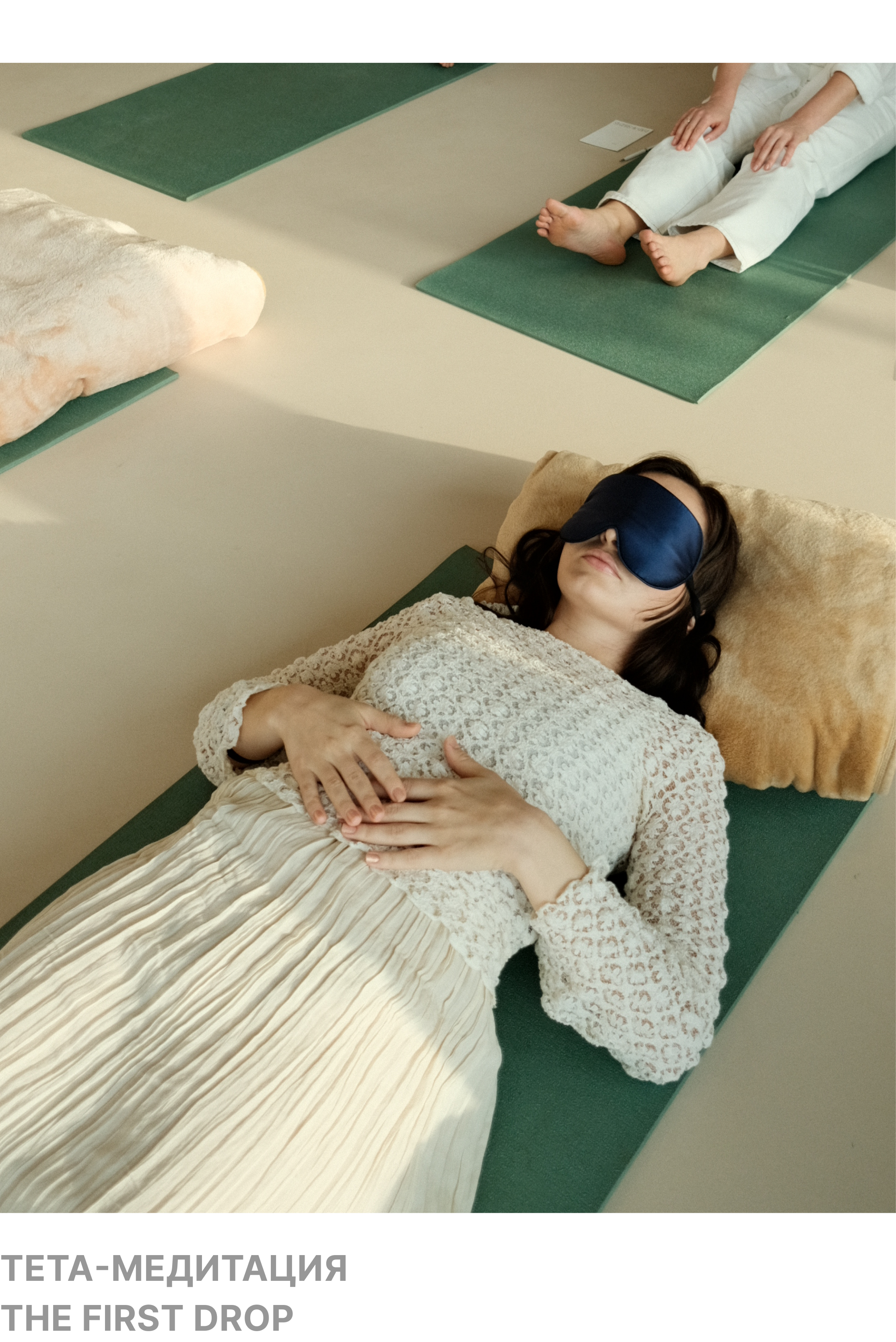 A woman wearing a sleep mask is lying peacefully on a green mat, with her hands resting on her chest. She is dressed in a lace top and a pleated skirt, with her head on a pillow.