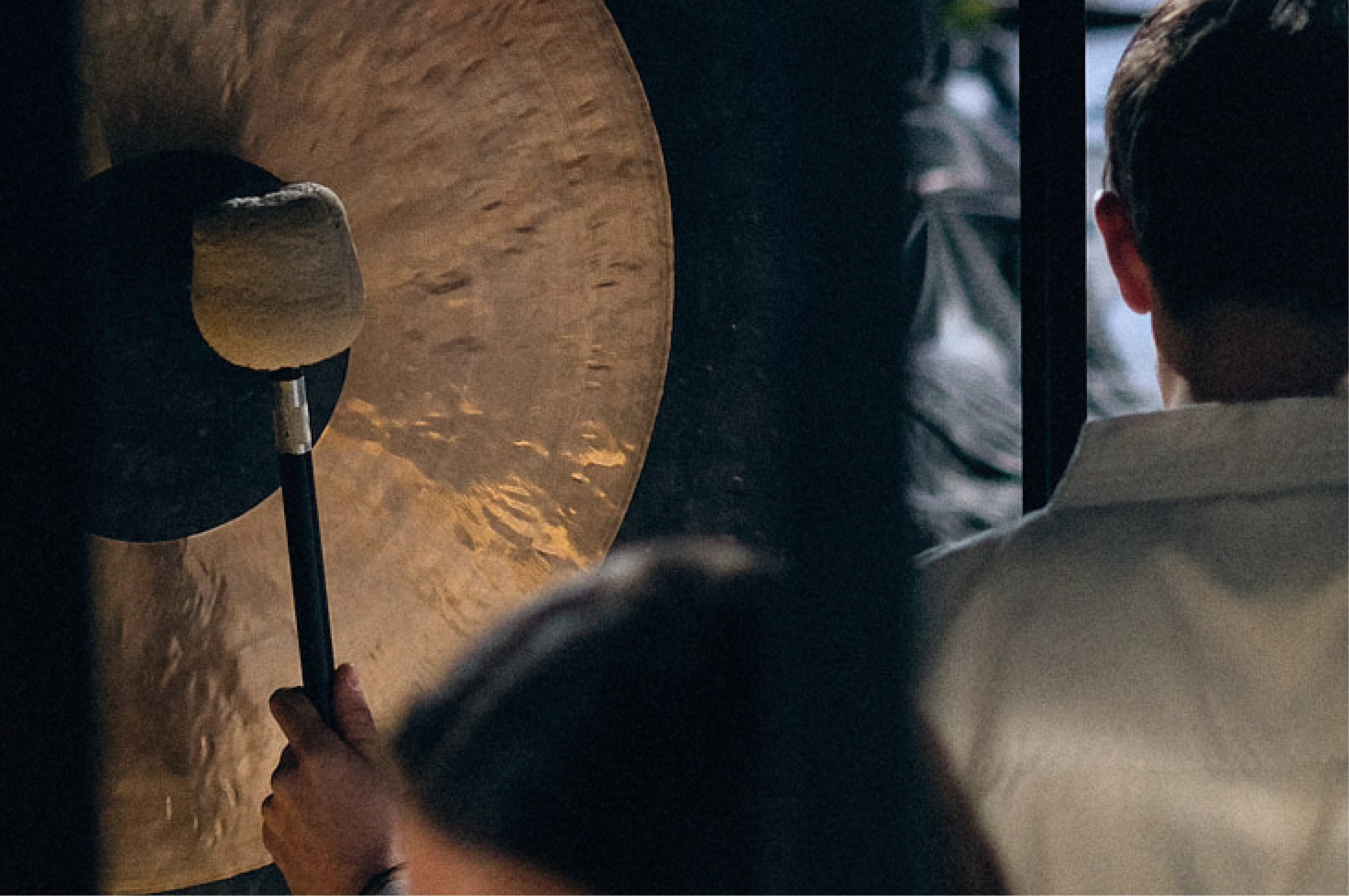 Person hitting a gong with a mallet in a dimly lit room.