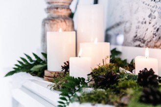 Image of candles displayed ontop of fireplace with greenery surrounding the candles