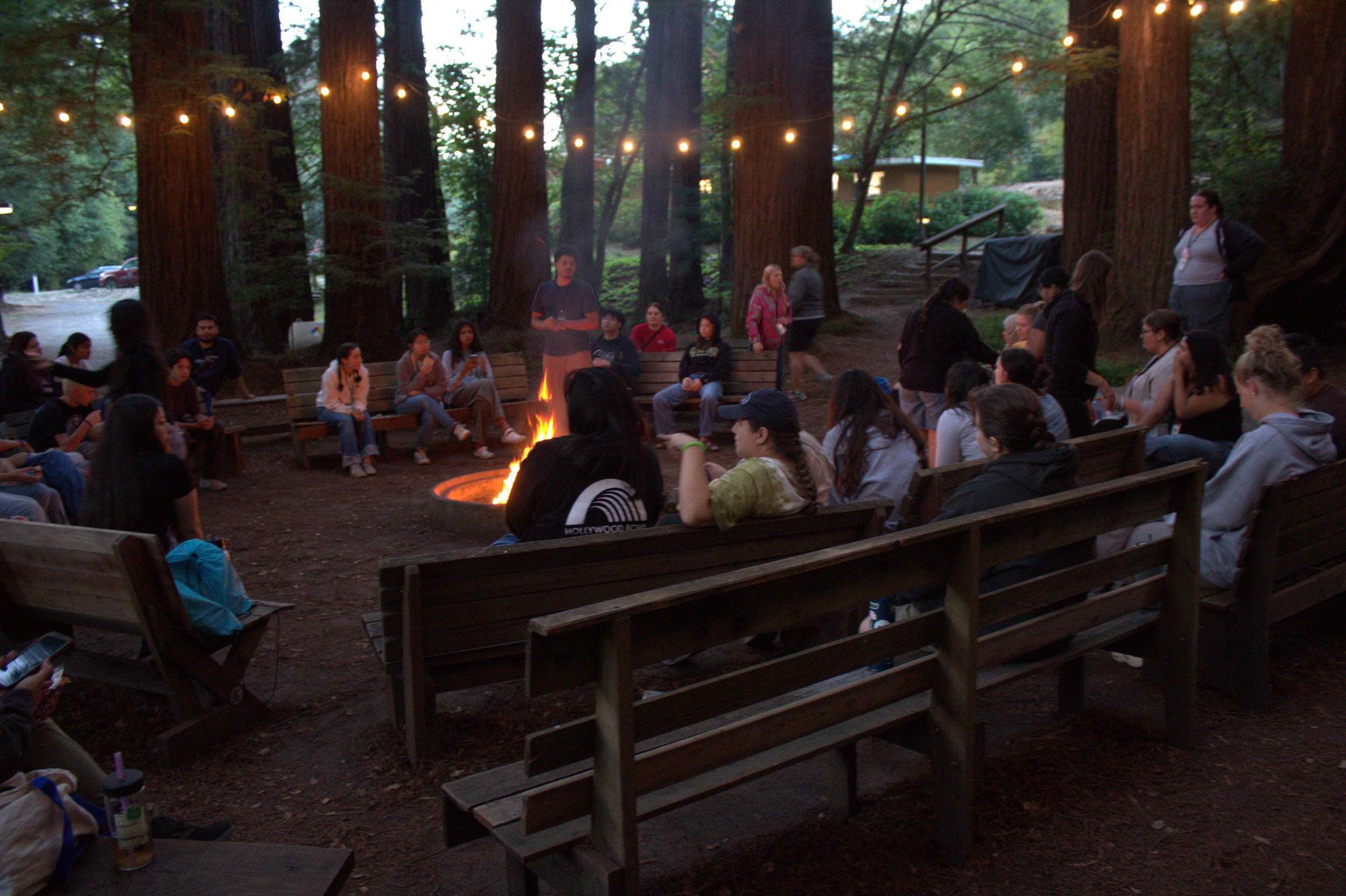 Image of Statewide Youth Advocacy Conference attendees around a lit campfire playing games as the sun is setting.