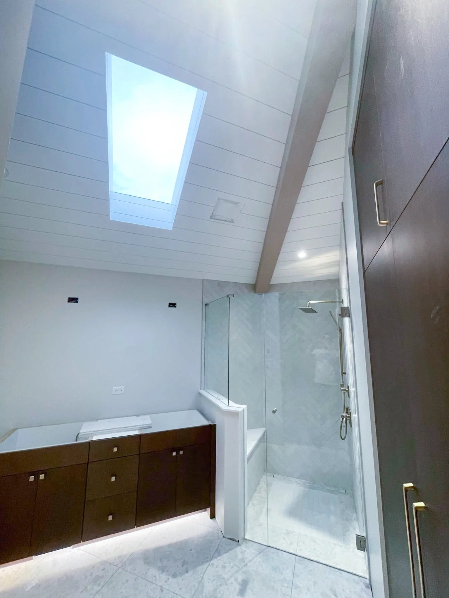Modern bathroom with a skylight, shower area with glass enclosure, dark wood cabinet, and white walls.