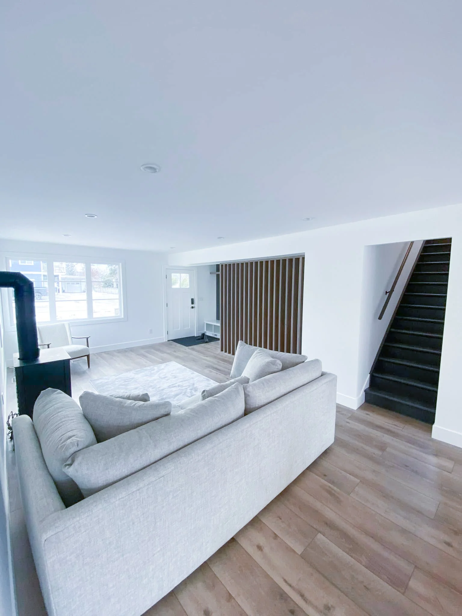 Living room with a beige sofa, wooden floor, staircase, and large window.