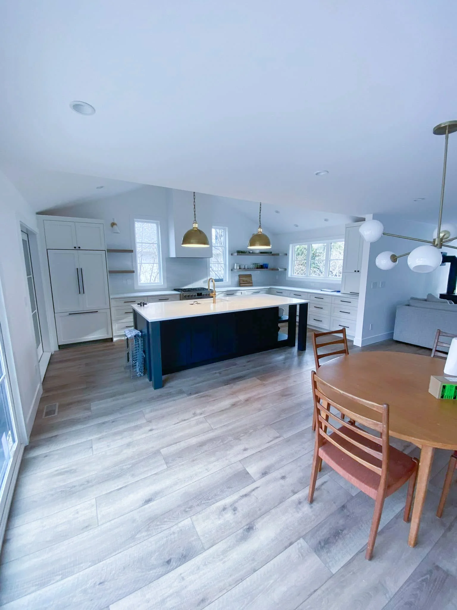 Modern kitchen with white cabinets, a dark island with a white countertop, three gold pendant lights, and a round wooden dining table with chairs.