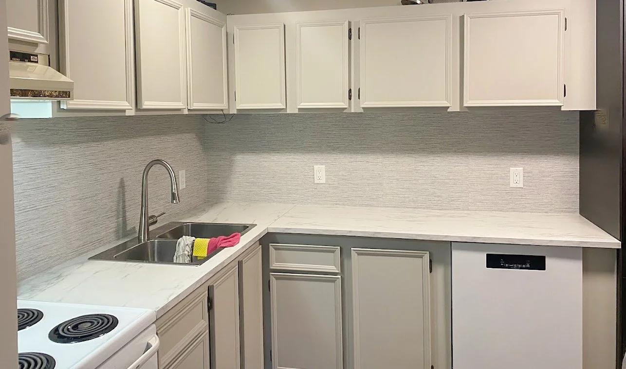 Kitchen with white cabinets, marble countertop, double sink with cleaning cloth, electric stove, and dishwasher.