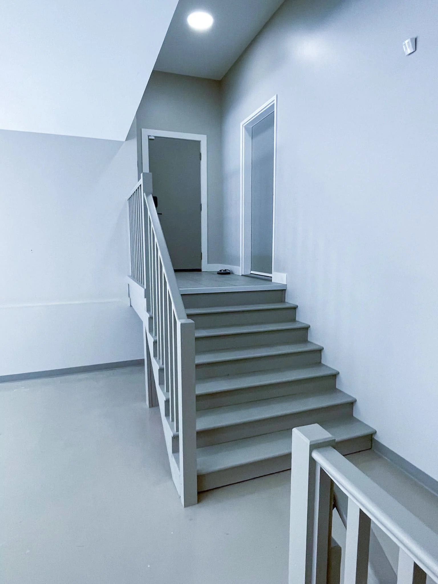 Interior view of a staircase with white railings, leading to a landing with a closed door and a sliding door on white walls.