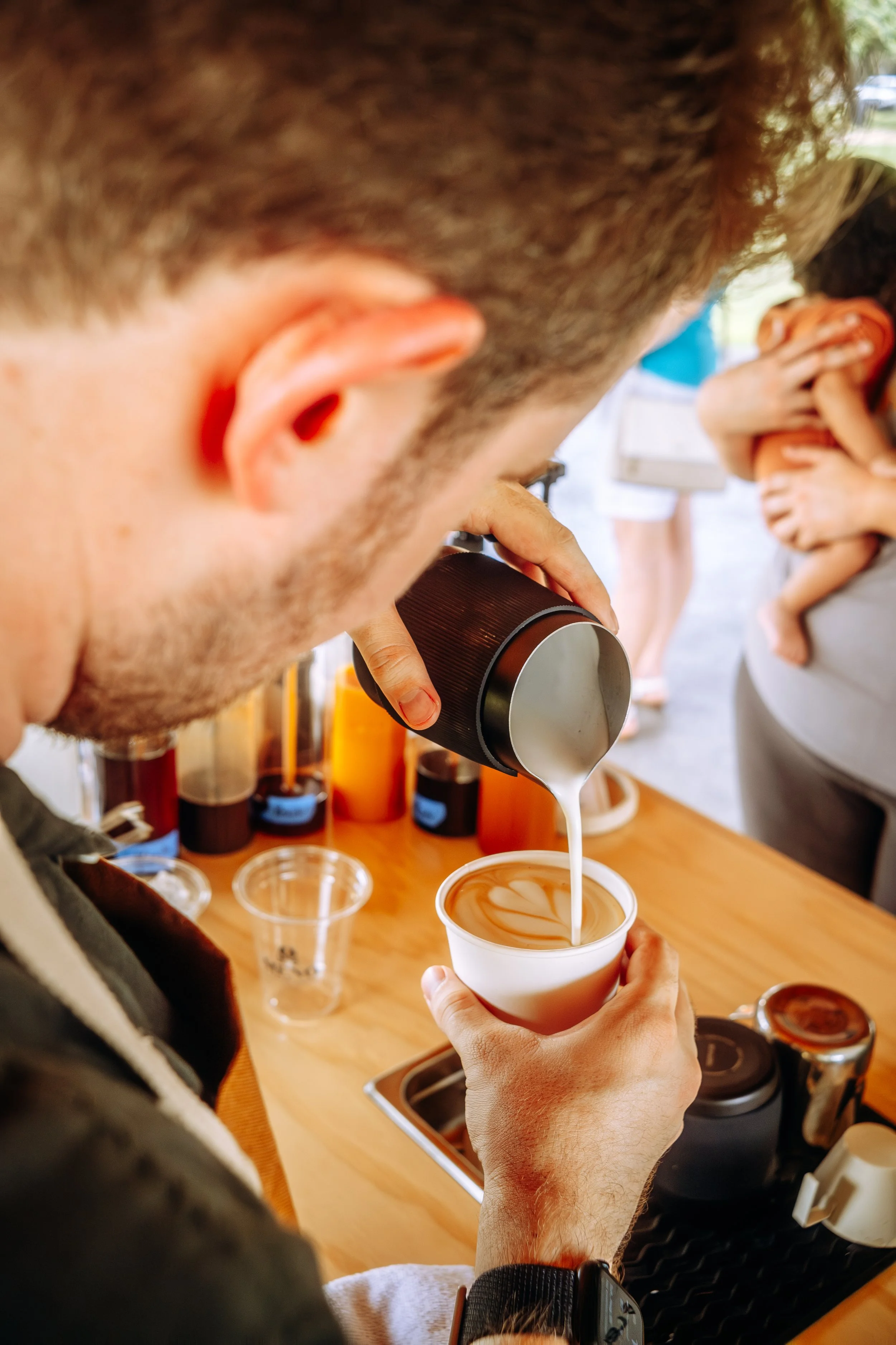 A man preparing a latte art coffee at a counter surrounded by various coffee-making supplies. Coffee Catering in Houston, Texas Coffee Cart and Mobile Espresso Bar Event Baristas. Coffee Vendor services