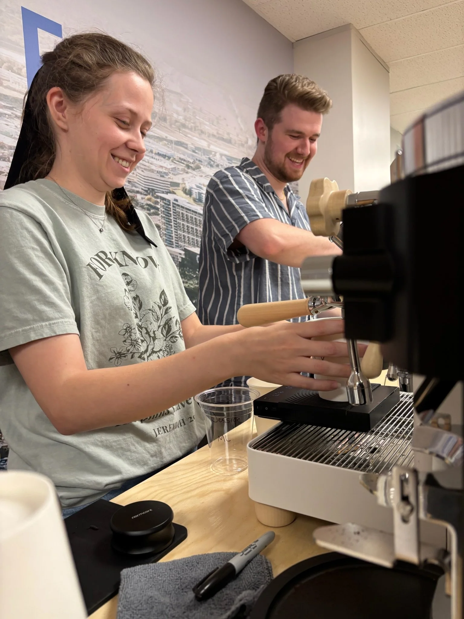 Two smiling people operating a coffee espresso machine behind Meno Coffee Cart