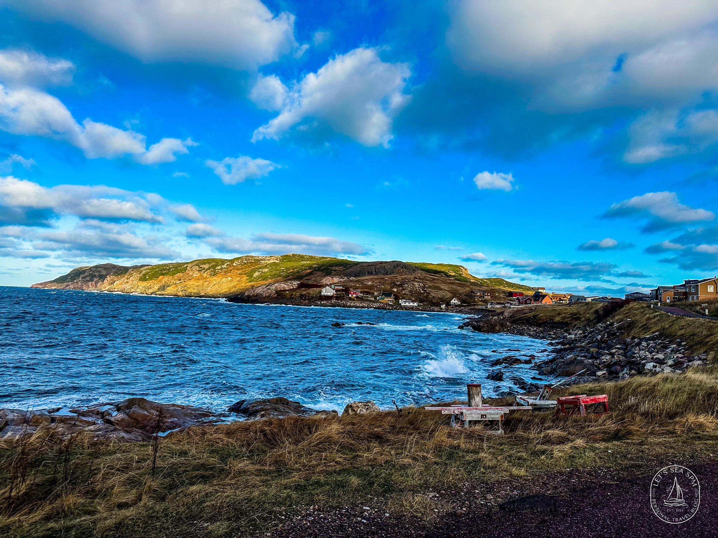 Coastal landscape view in Saint Pierre and Miquelon with ocean cliffs, colorful homes, and dramatic Atlantic clouds near Newfoundland.