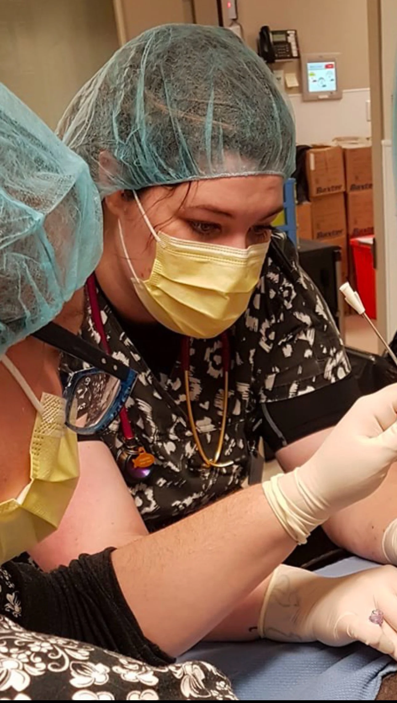 Former veterinary technical assistant performing a medical procedure while wearing protective equipment in a clinical setting.