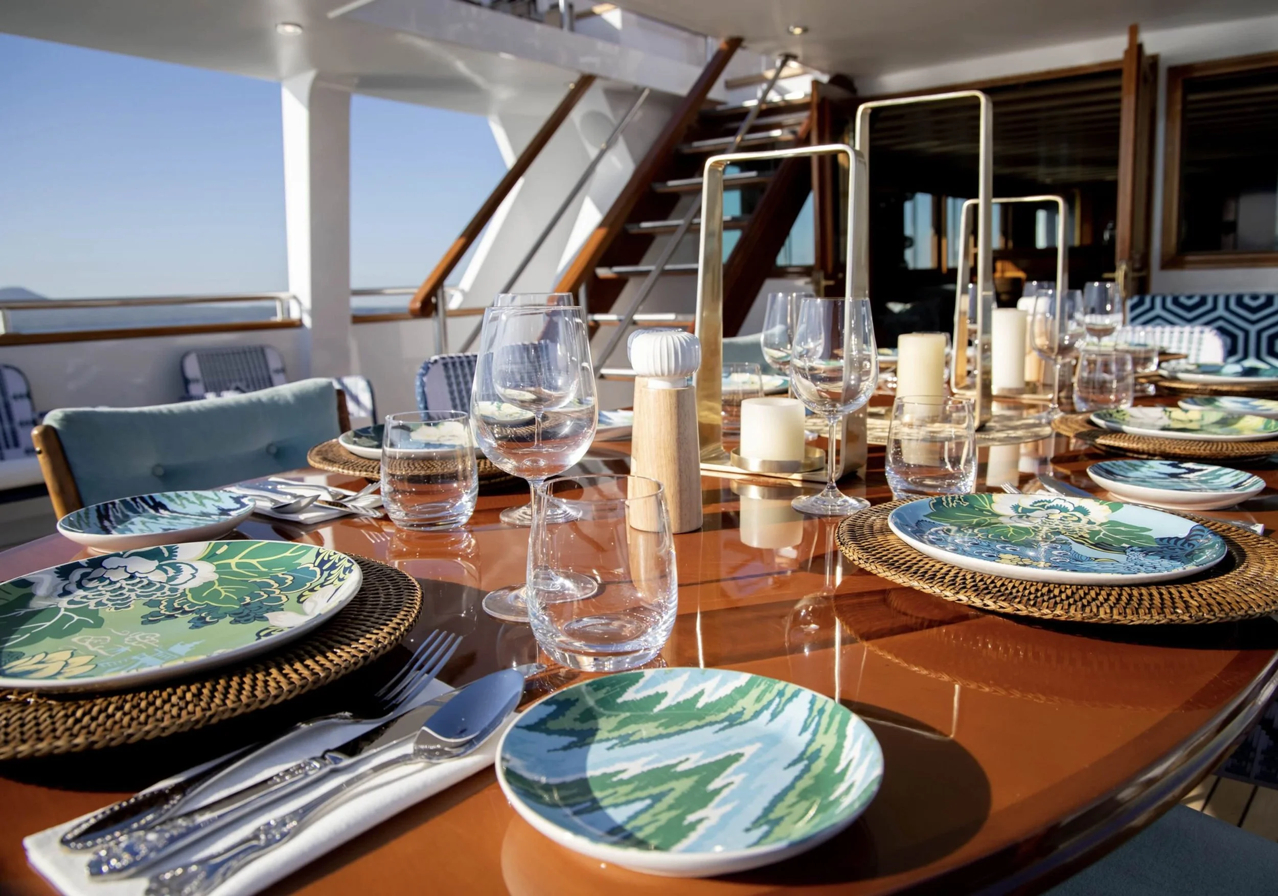 Dining table set with colorful plates, glassware, cutlery, candles, and decorative elements on a yacht outdoor deck.
