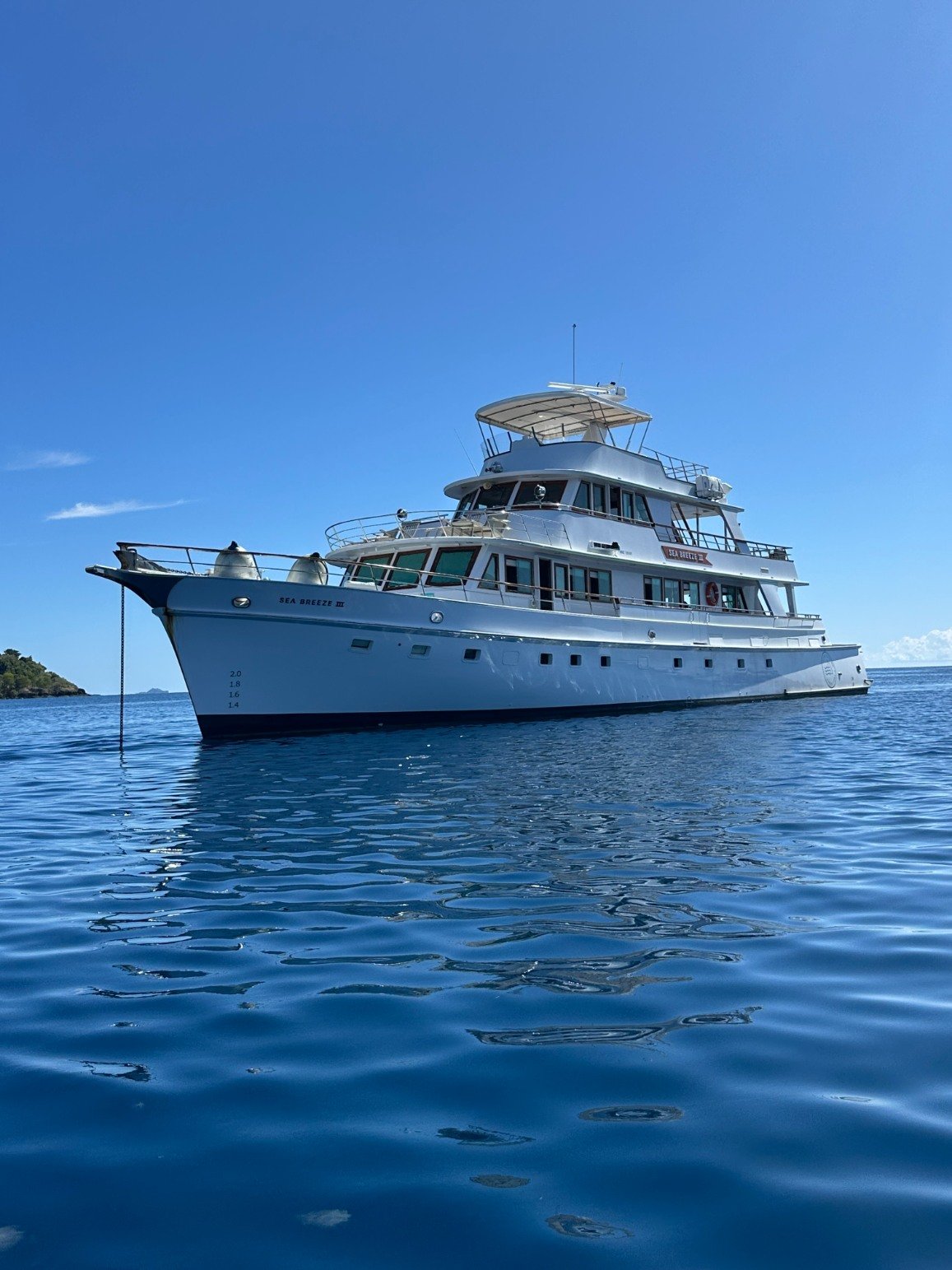 A large white yacht floating on calm blue ocean water under a clear blue sky.