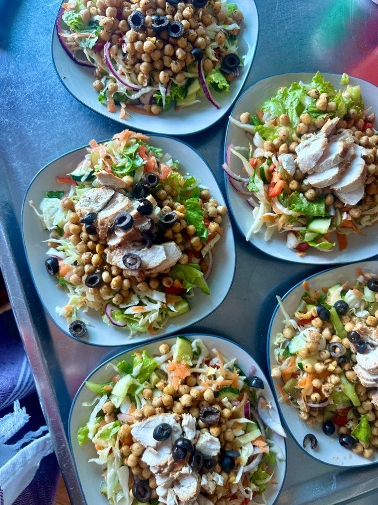 Five plates of mixed salads with chickpeas, sliced grilled chicken, black olives, and chopped vegetables like lettuce, cucumbers, and tomatoes.