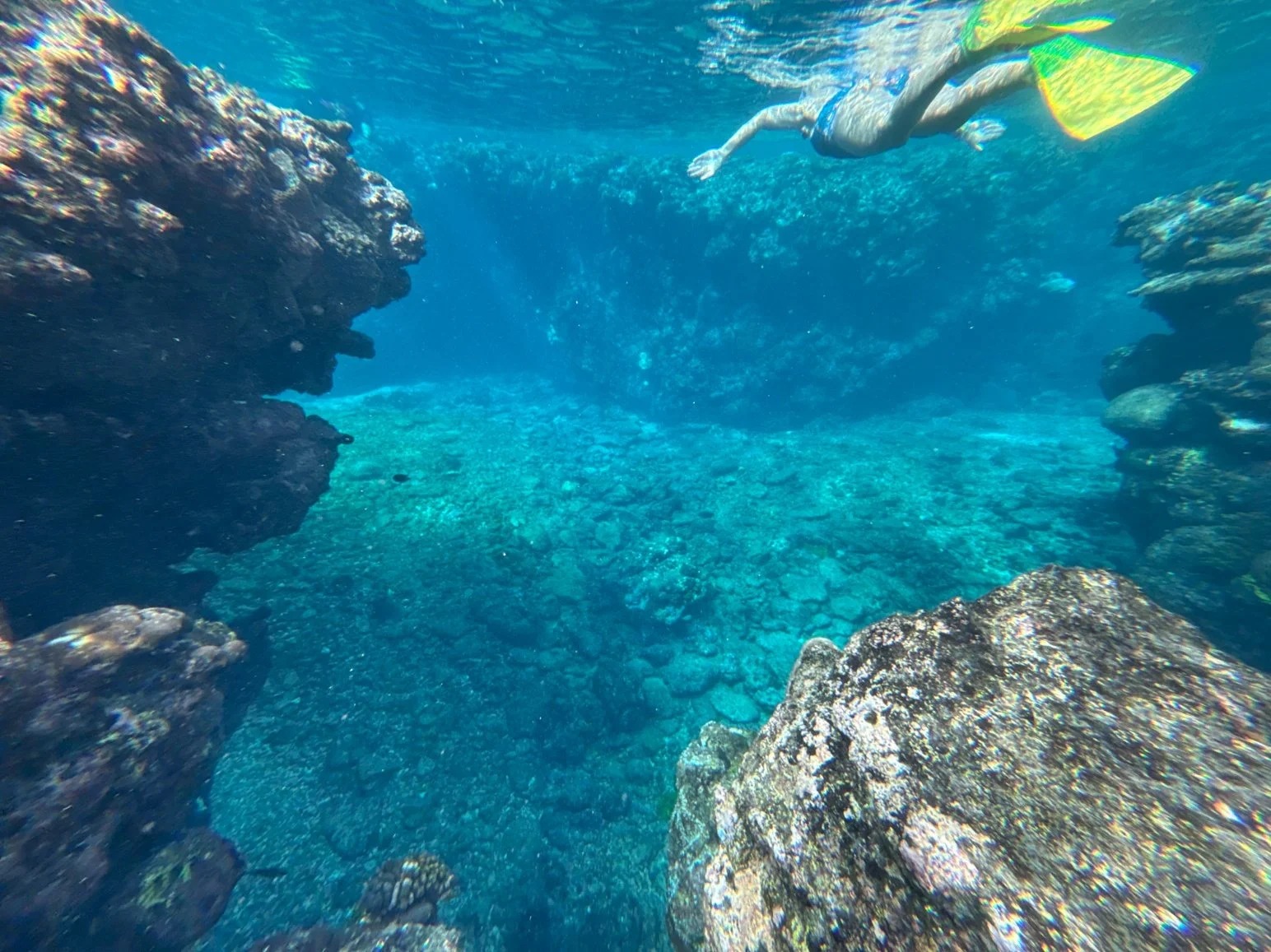 A person snorkeling underwater near rocks in a clear blue ocean.