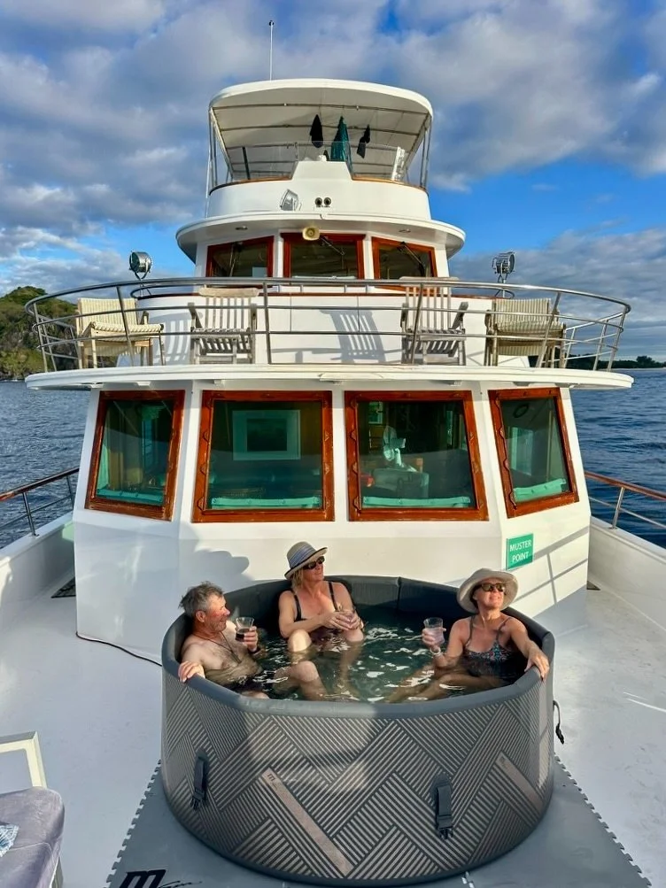 Three older adults relaxing in a hot tub on the deck of a boat, with the boat's cabin and the water in the background.