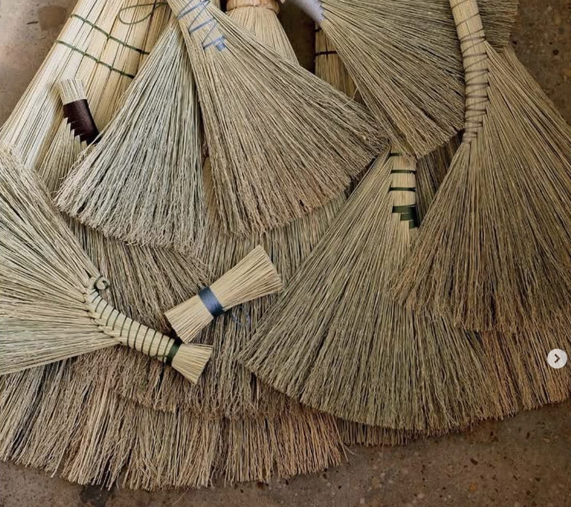Collection of straw brooms with different sizes and shapes arranged on a surface.