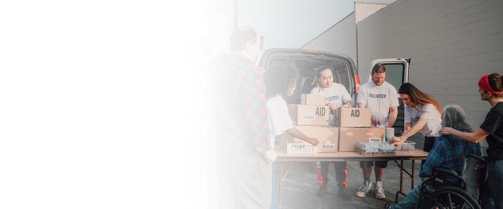 Volunteers packing supplies such as food, medicine, and aid into boxes outdoors next to a van.