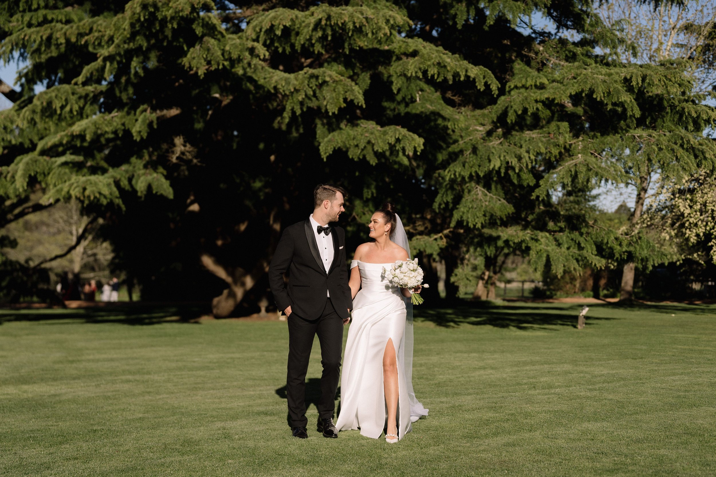 Bride and groom walking on grass under large tree