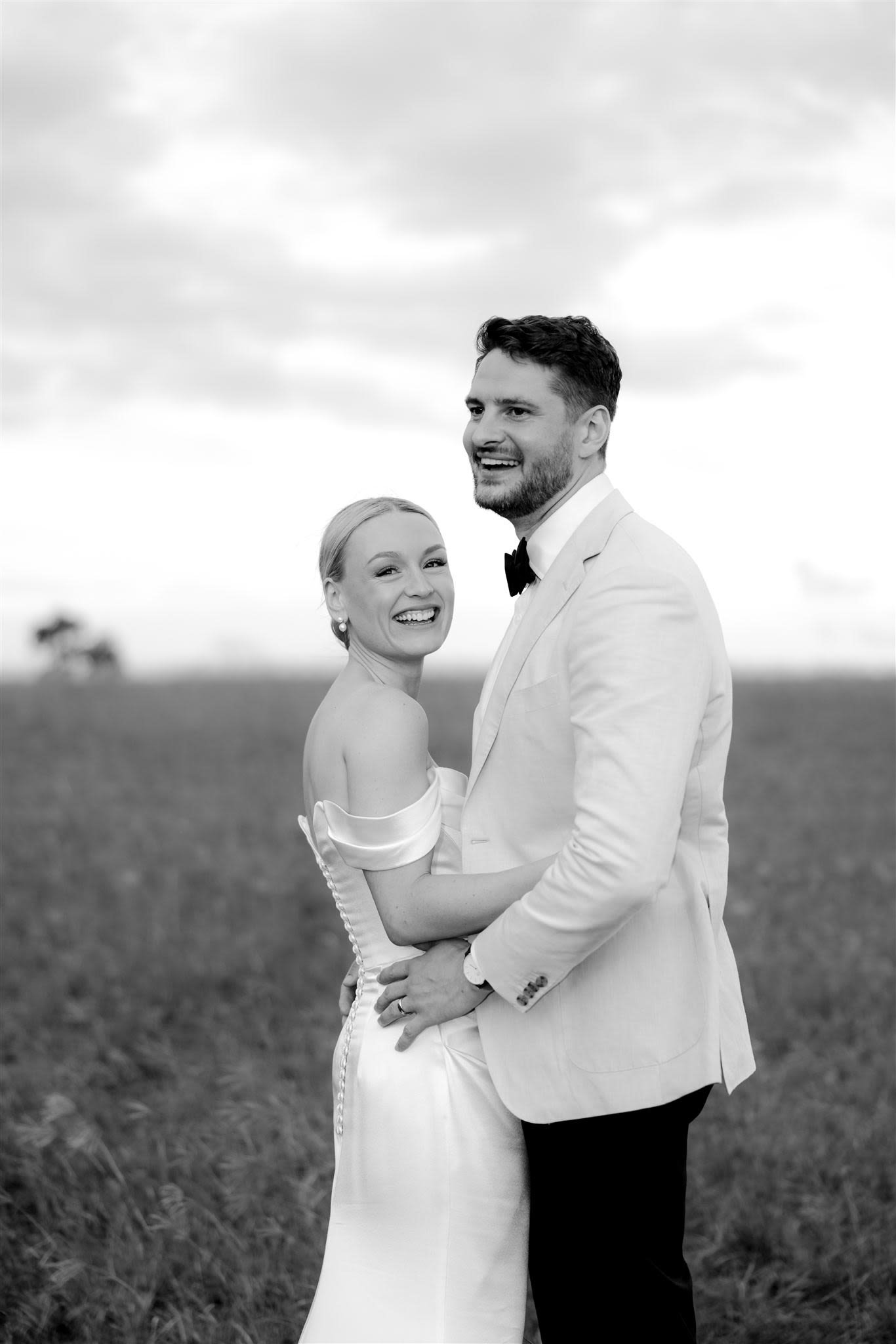 Black and white photo of a smiling couple in formal attire, outdoors.