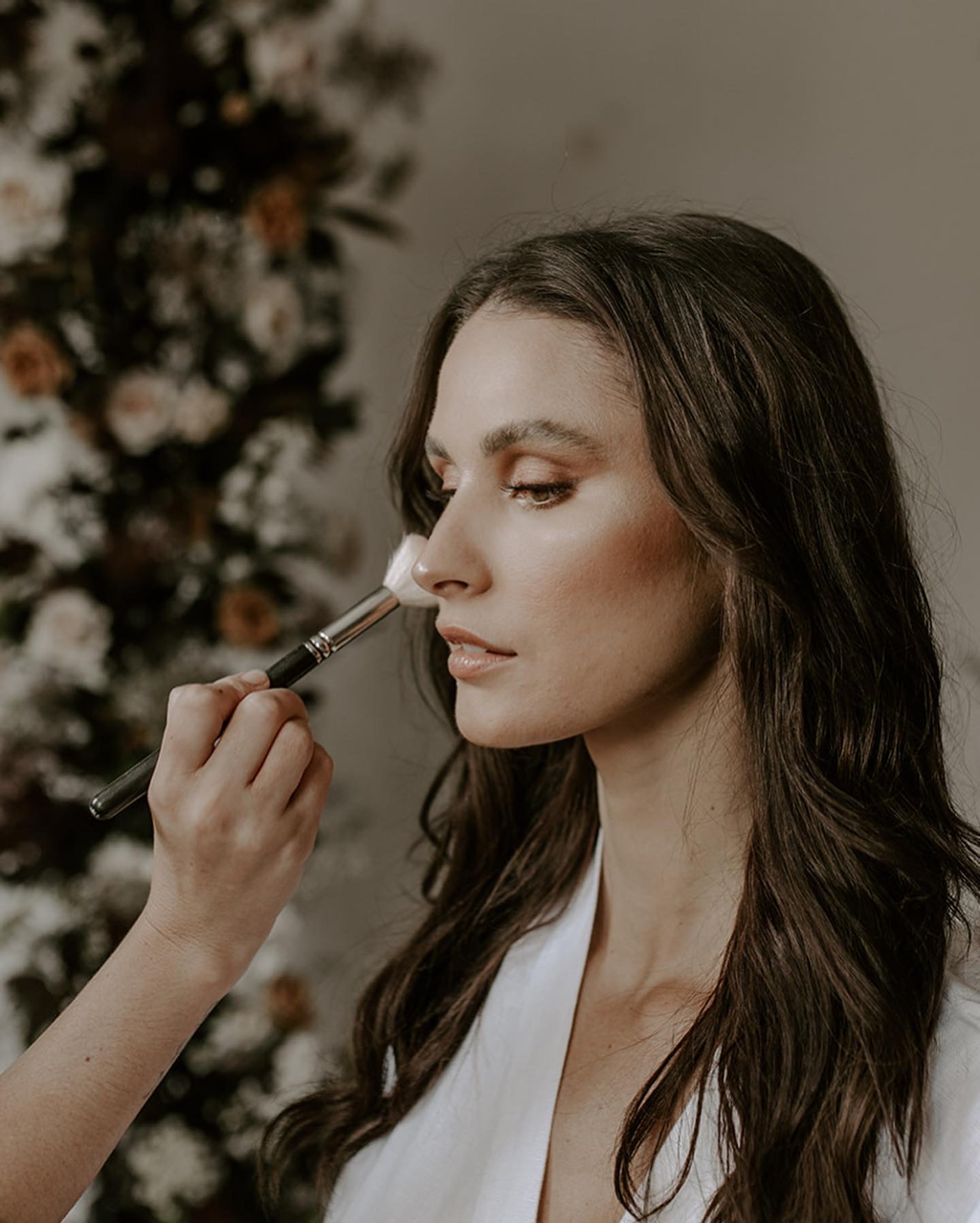 Person receiving makeup application with a brush, floral background.