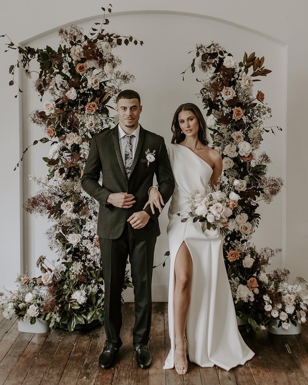 Bride and groom posing in elegant attire with floral backdrop