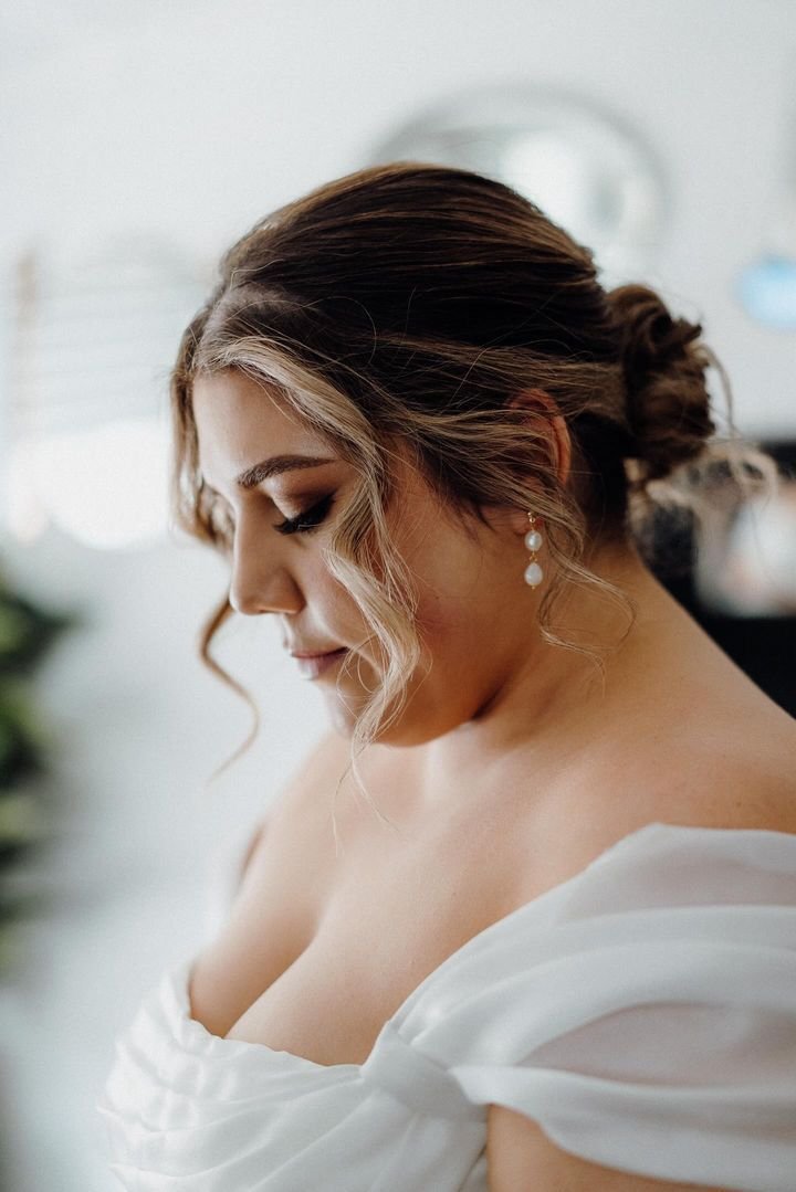 Bride with elegant updo and pearl earrings in a white gown.
