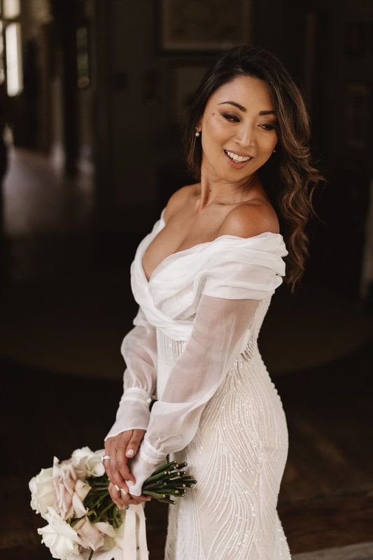Bride in white dress holding bouquet of roses indoors.