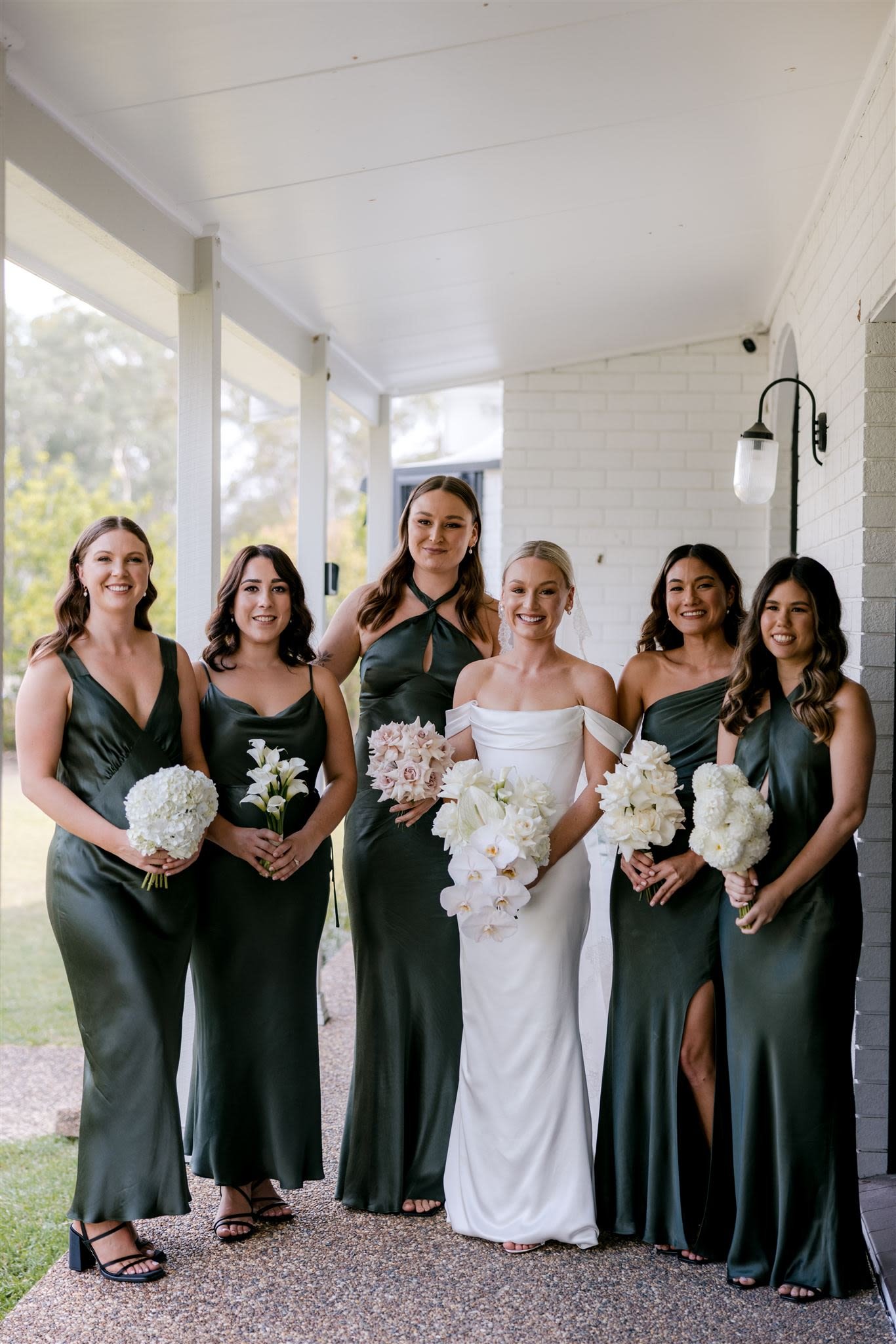 Bridal party with bridesmaids in dark green dresses and bride in a white dress holding bouquets.